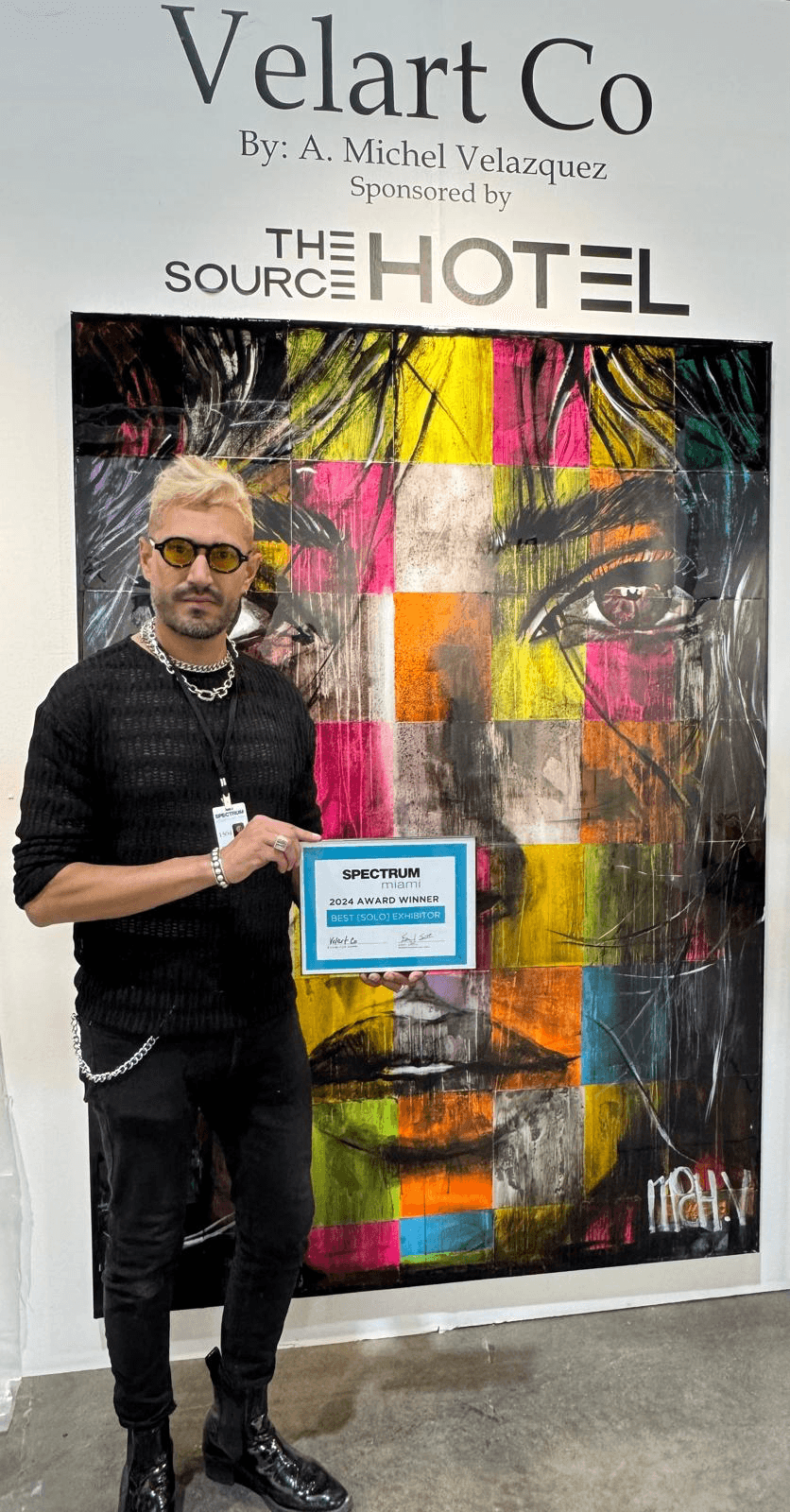 Person holding a certificate in front of colorful abstract artwork at Velart Co exhibition.