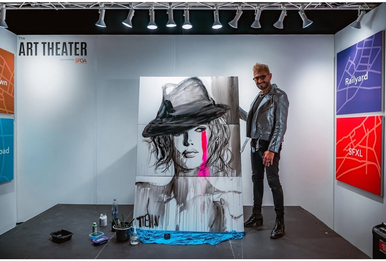 Person standing next to a large painting of a woman with a hat and pink lips, art gallery setting.
