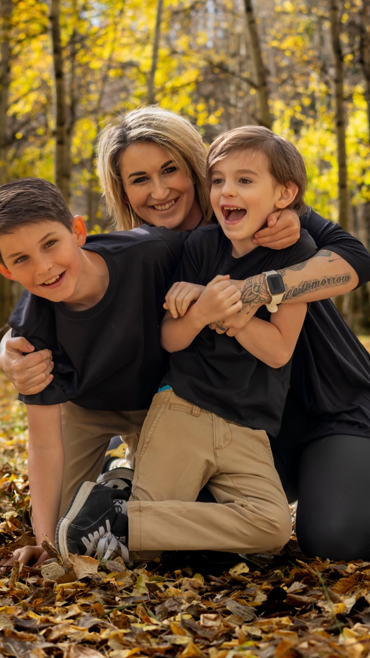 Woman with two children outdoors in autumn, smiling and playing among fallen leaves.