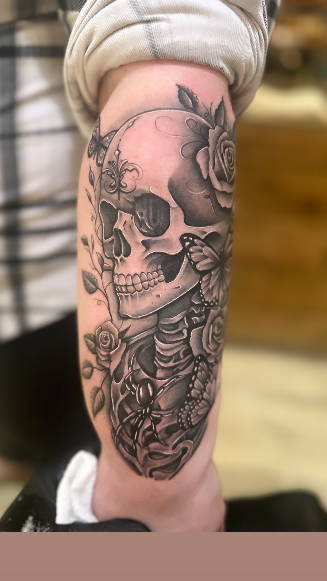 Tattoo of a skull with roses and a skeleton on a person's arm.