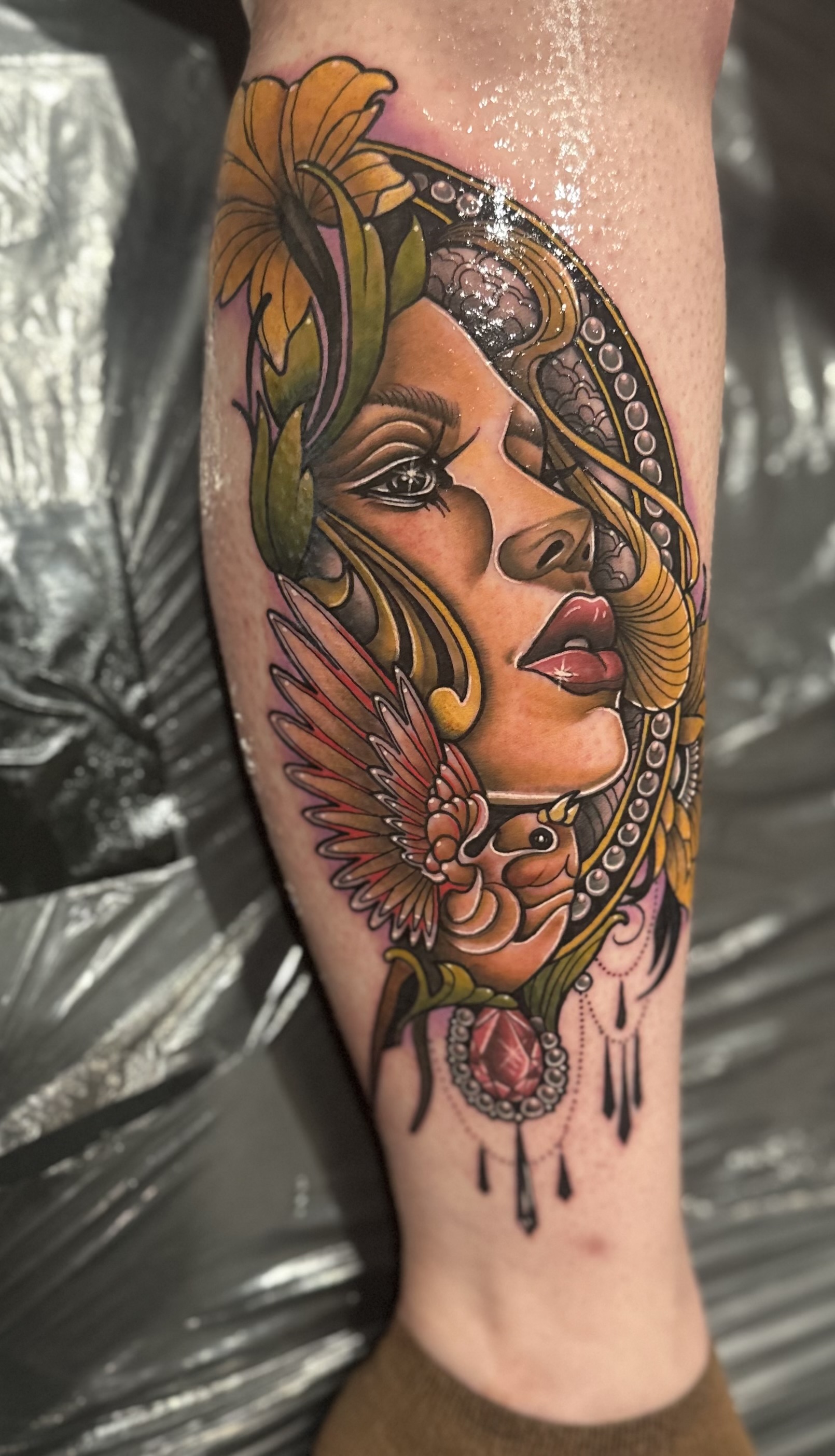 Tattoo of a woman's face with flowers, a bird, and decorative elements on a person's leg.