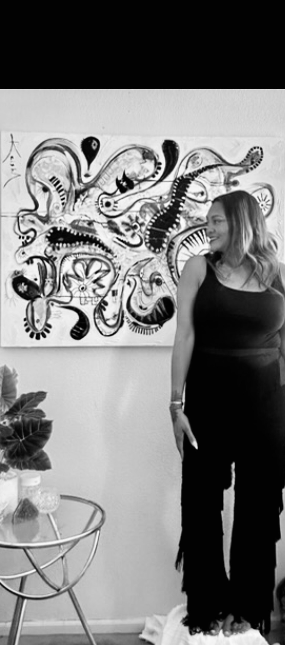 Woman standing next to an abstract black and white artwork on the wall, holding a phone in her right hand.