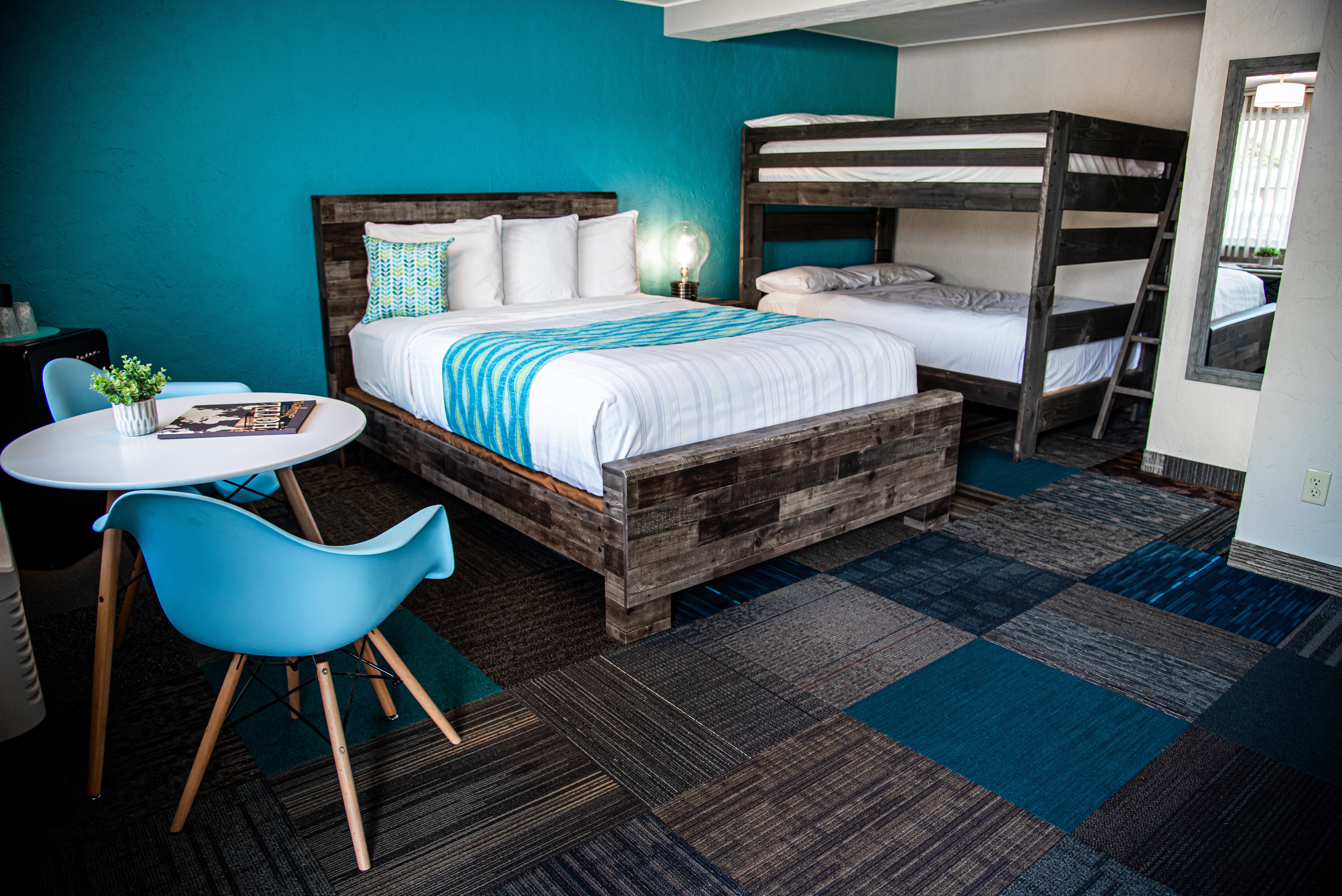 Room with a bed, bunk bed, table, and blue chair, with a blue wall and patterned carpet.