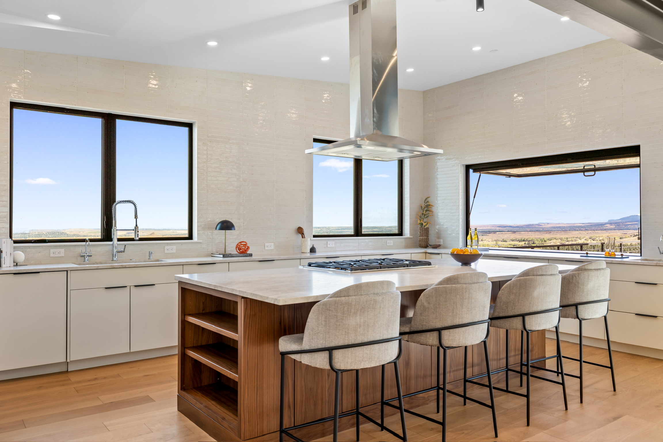 Modern kitchen with large windows, white cabinets, a central island with seating, and a view outside.