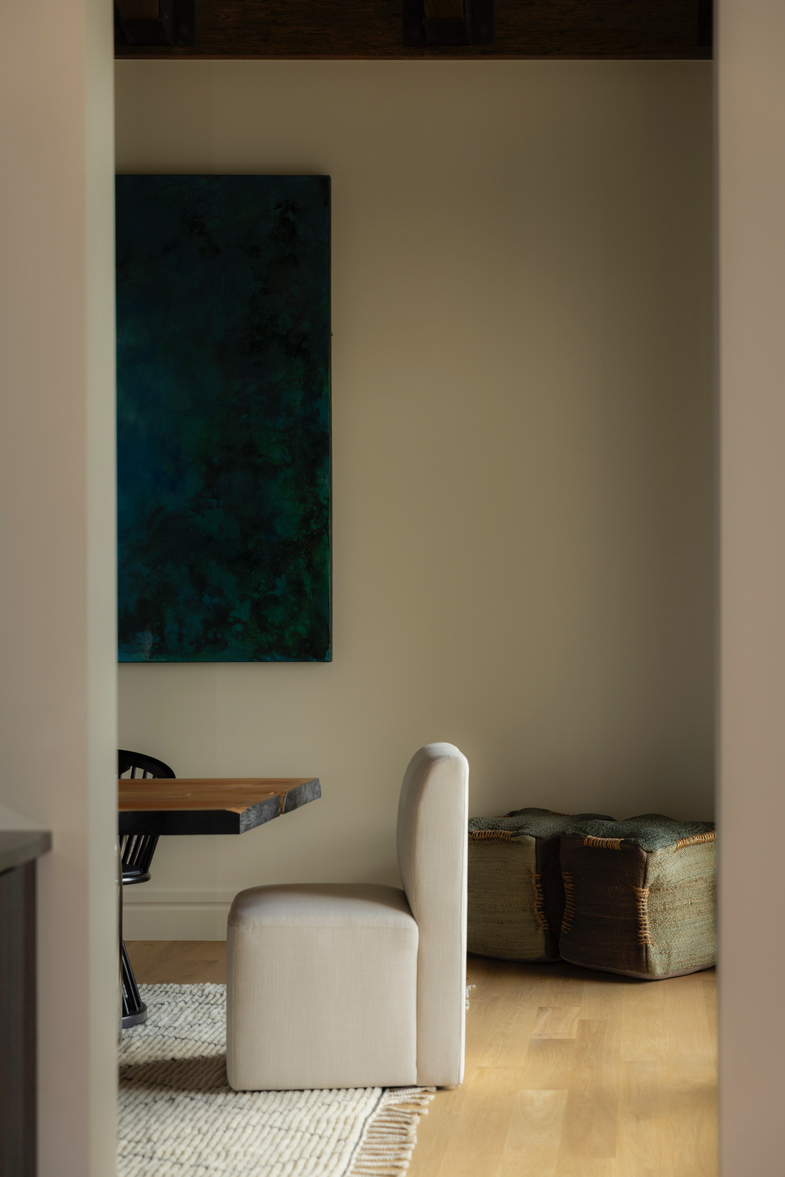 Interior room with a white chair, a wooden table, a large green painting, and a wooden chest against the wall.