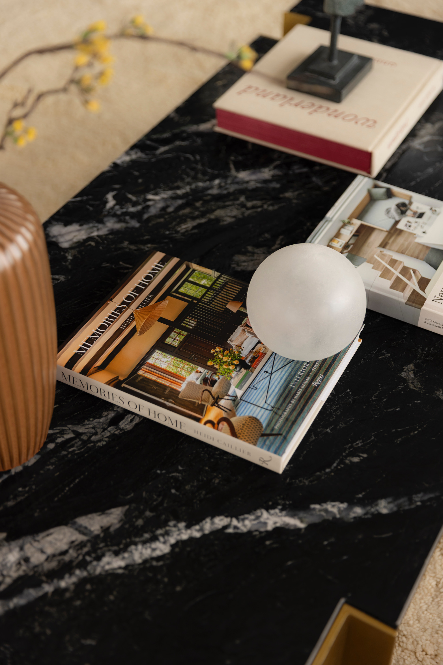 Open magazine with interior design images on a black marble table, a white spherical object, and a brown vase.