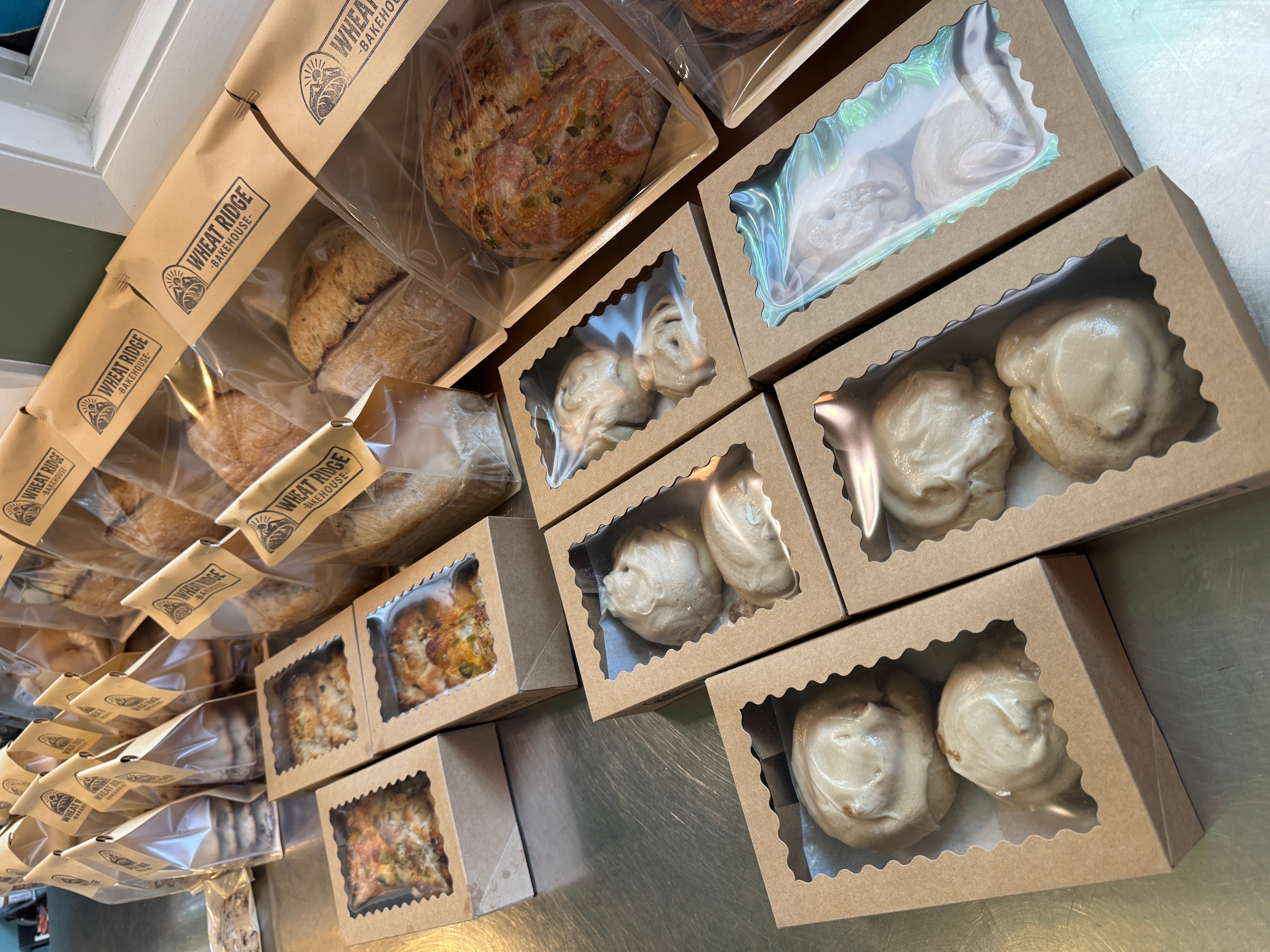 Boxes of baked goods, including cookies and pastries, arranged on a shelf with some in clear plastic containers.