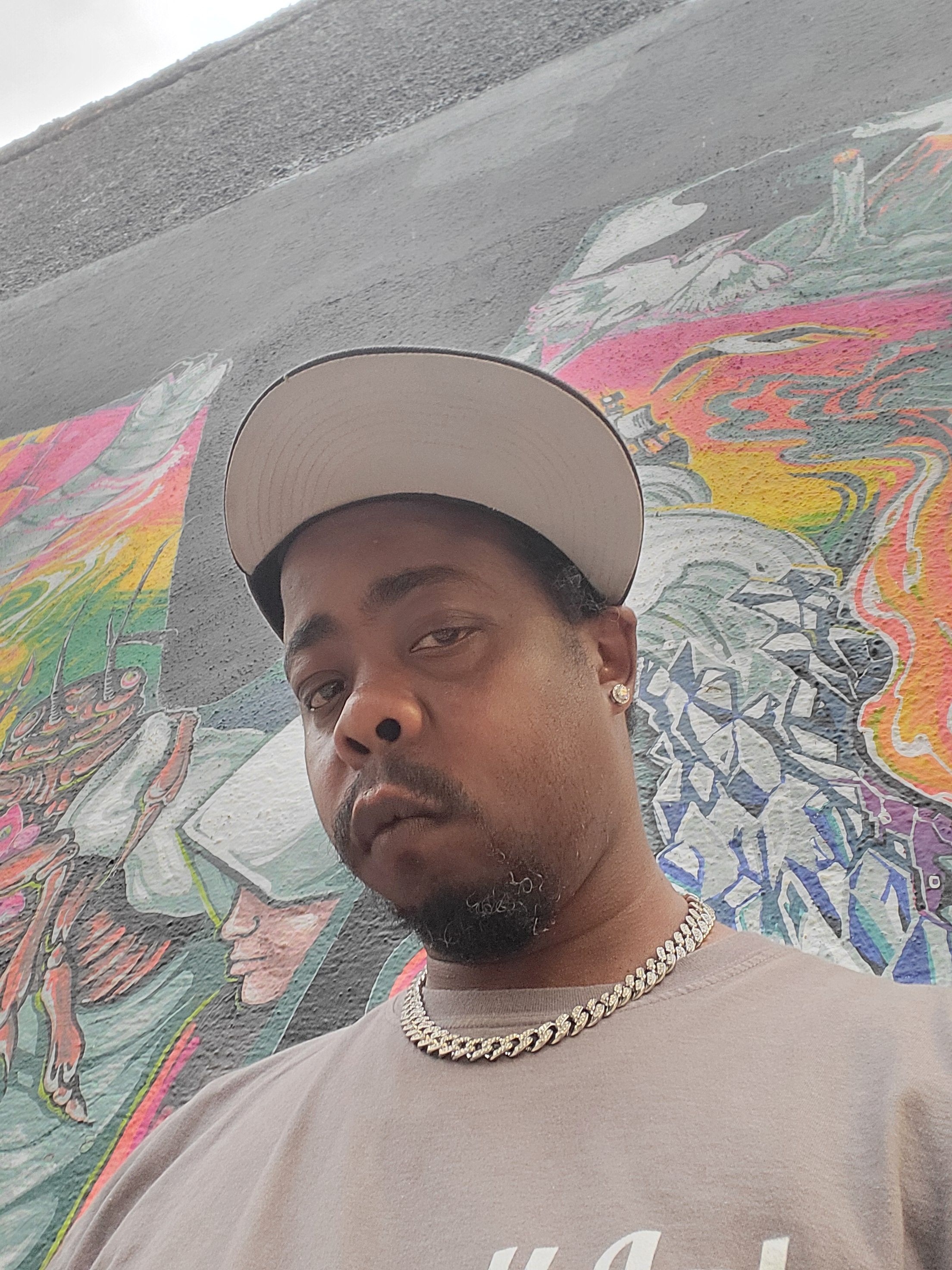 Man wearing a cap and pearl necklace, lying on colorful graffiti-covered ground, looking at the camera.
