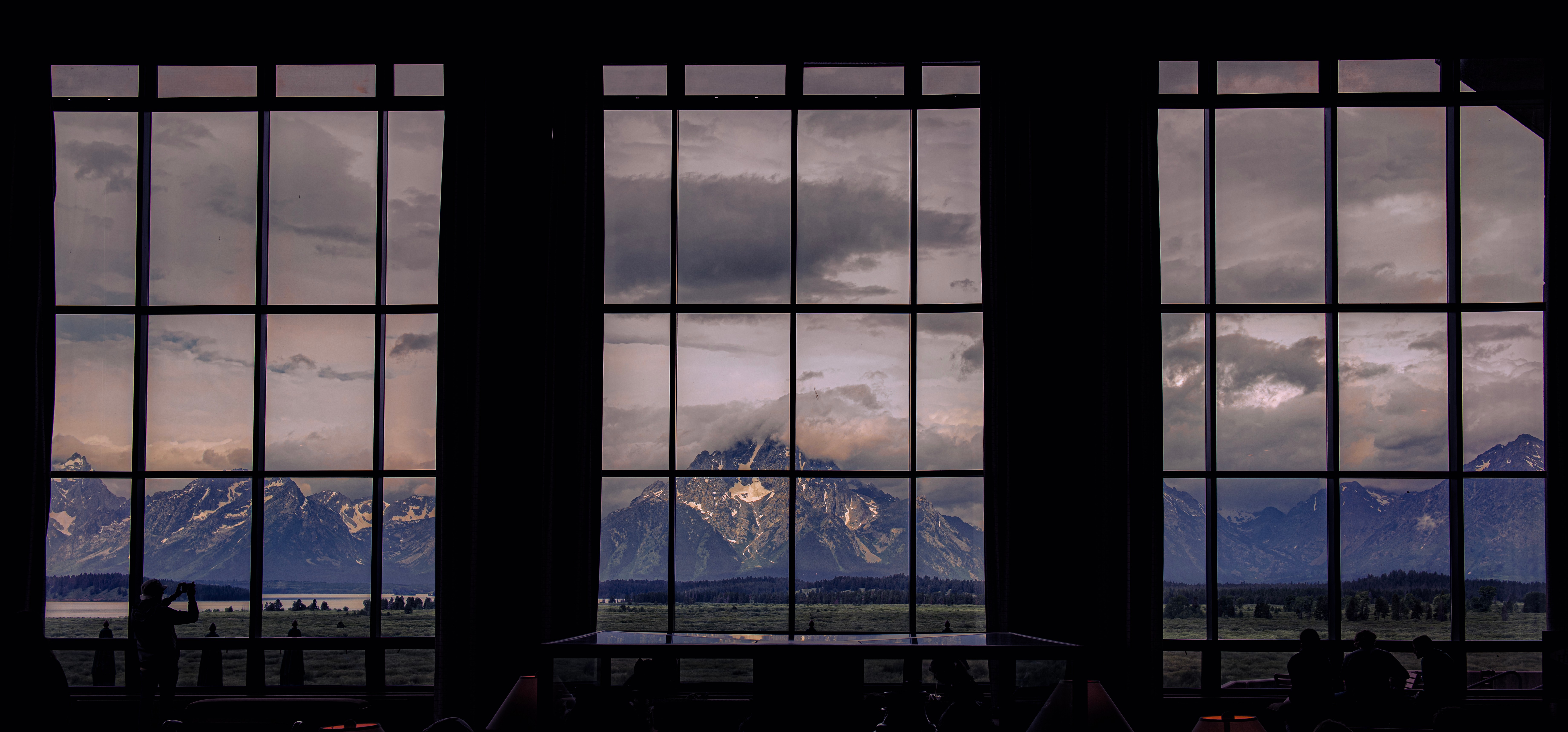 View through large windows showing mountains and cloudy sky, with dark interior in foreground.