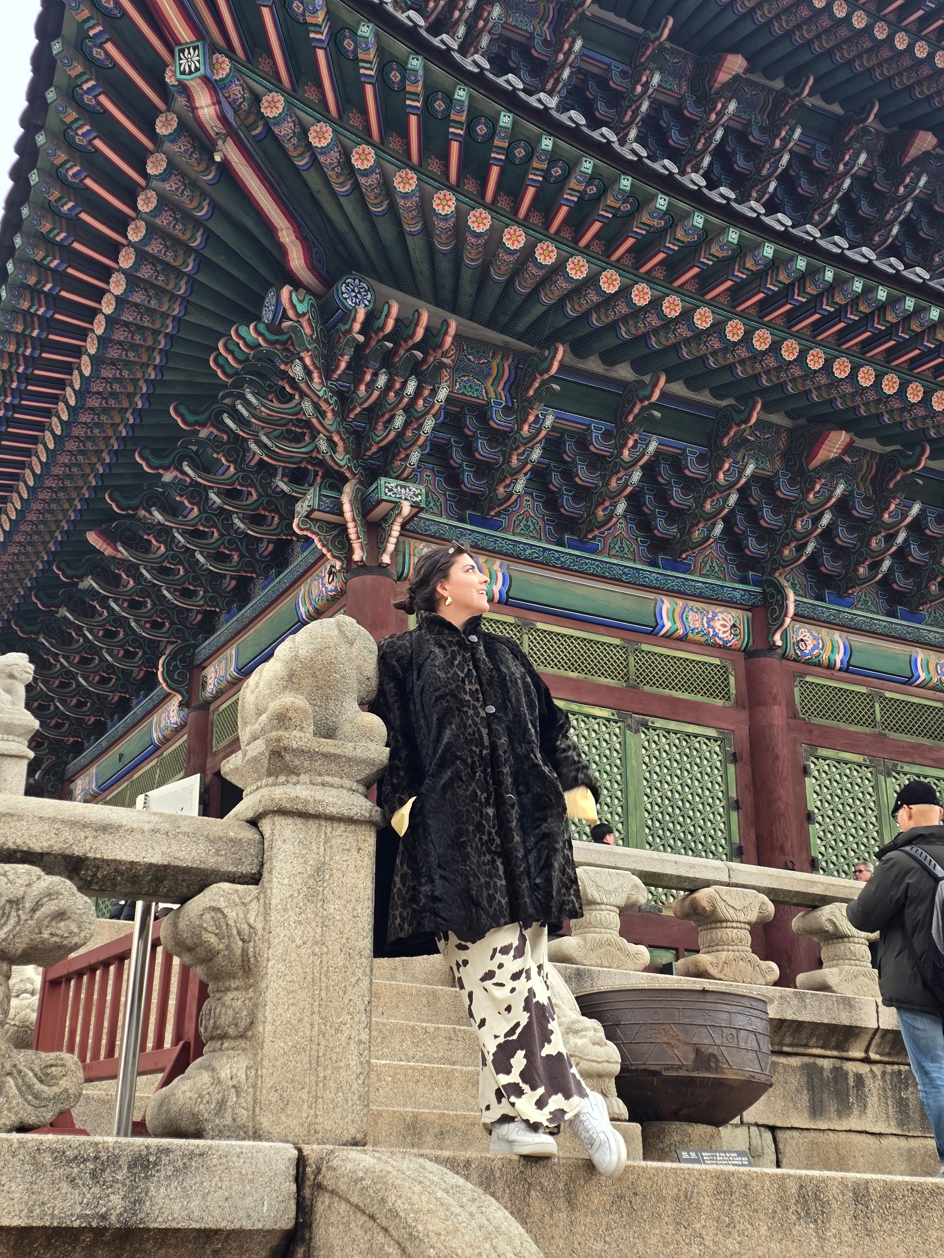 Person standing on stone railing with traditional Chinese roof structure overhead, colorful tiles and decorative elements.