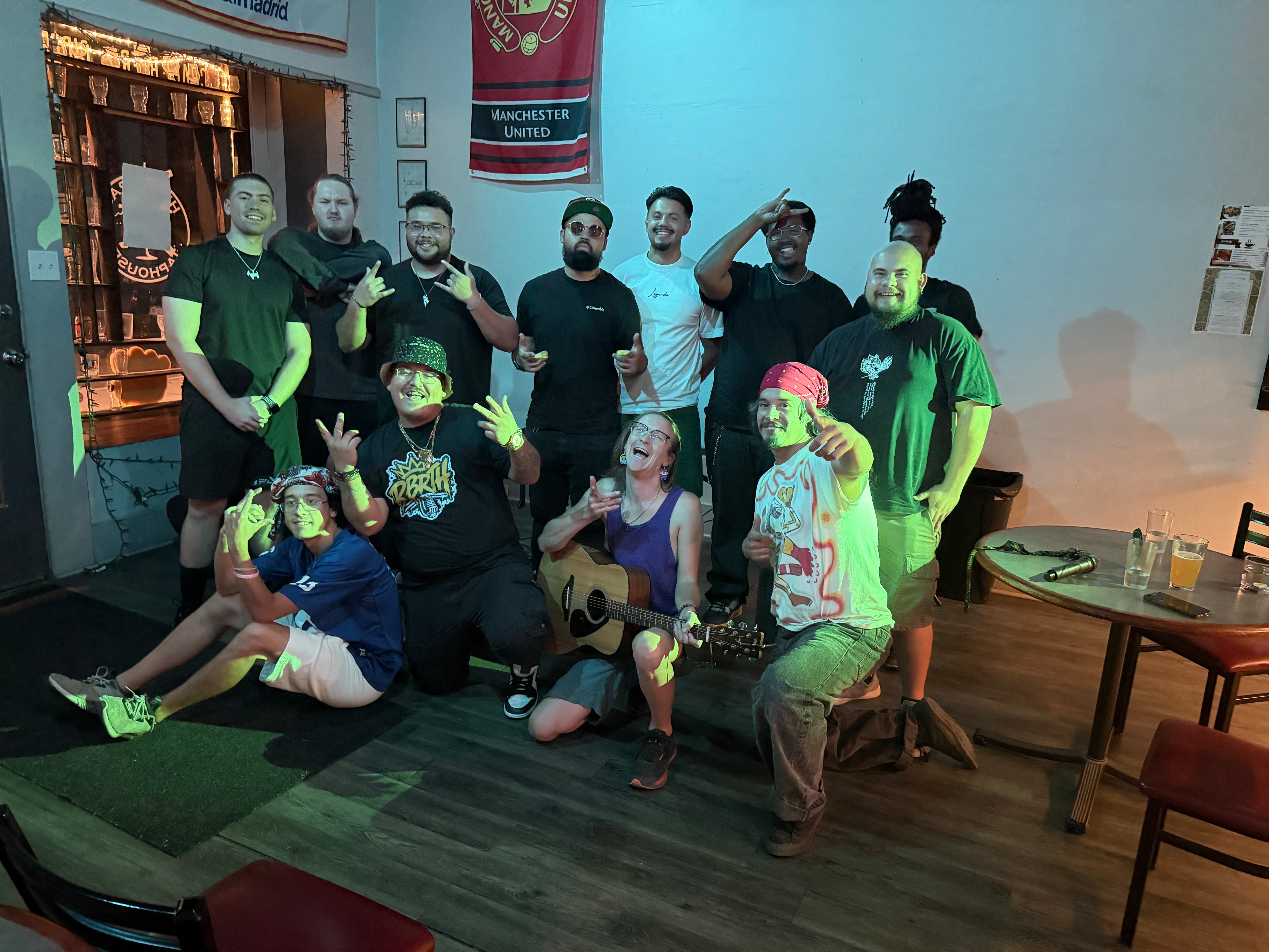 Group of ten people, some wearing masks, posing indoors with one person holding a guitar, in a room with wooden furniture.