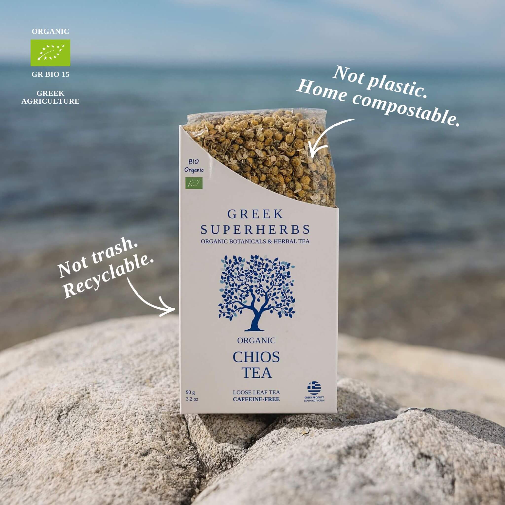 Box of Greek super herbs tea on rocks with ocean background, labeled as home compostable and recyclable, organic, with a tree logo.