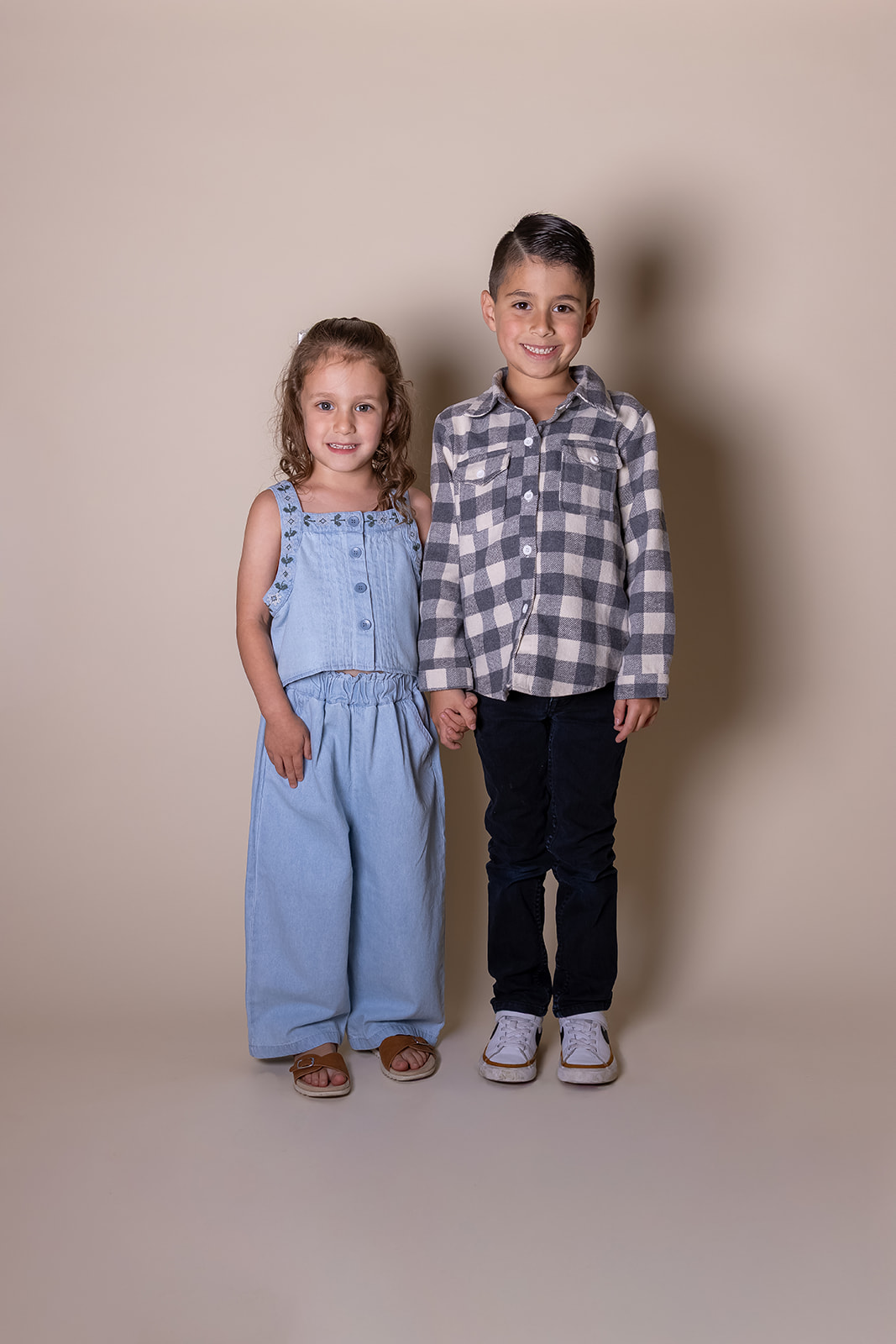 Two children, a girl and a boy, stand side by side against a plain background, smiling at the camera.