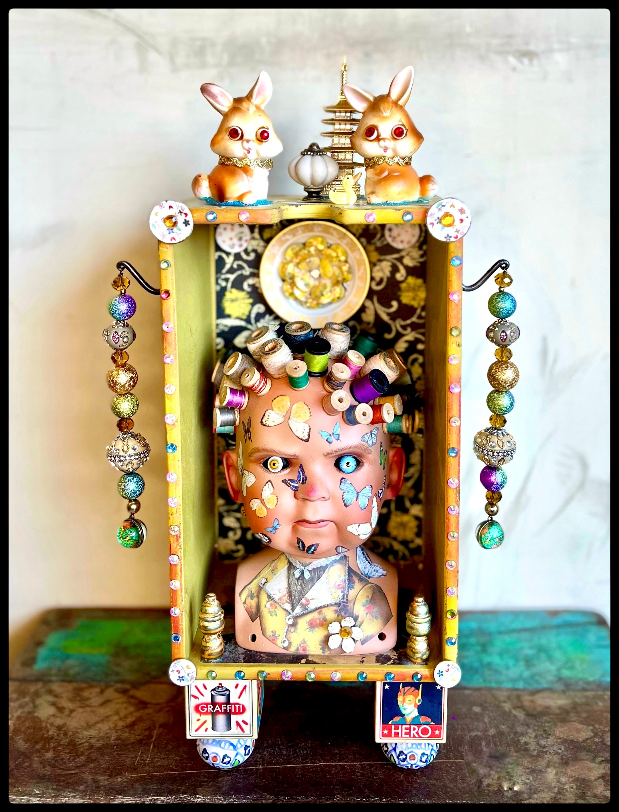 Decorative doll with a painted face, surrounded by colorful beads and ornaments, inside a decorated box with animal figurines on top.