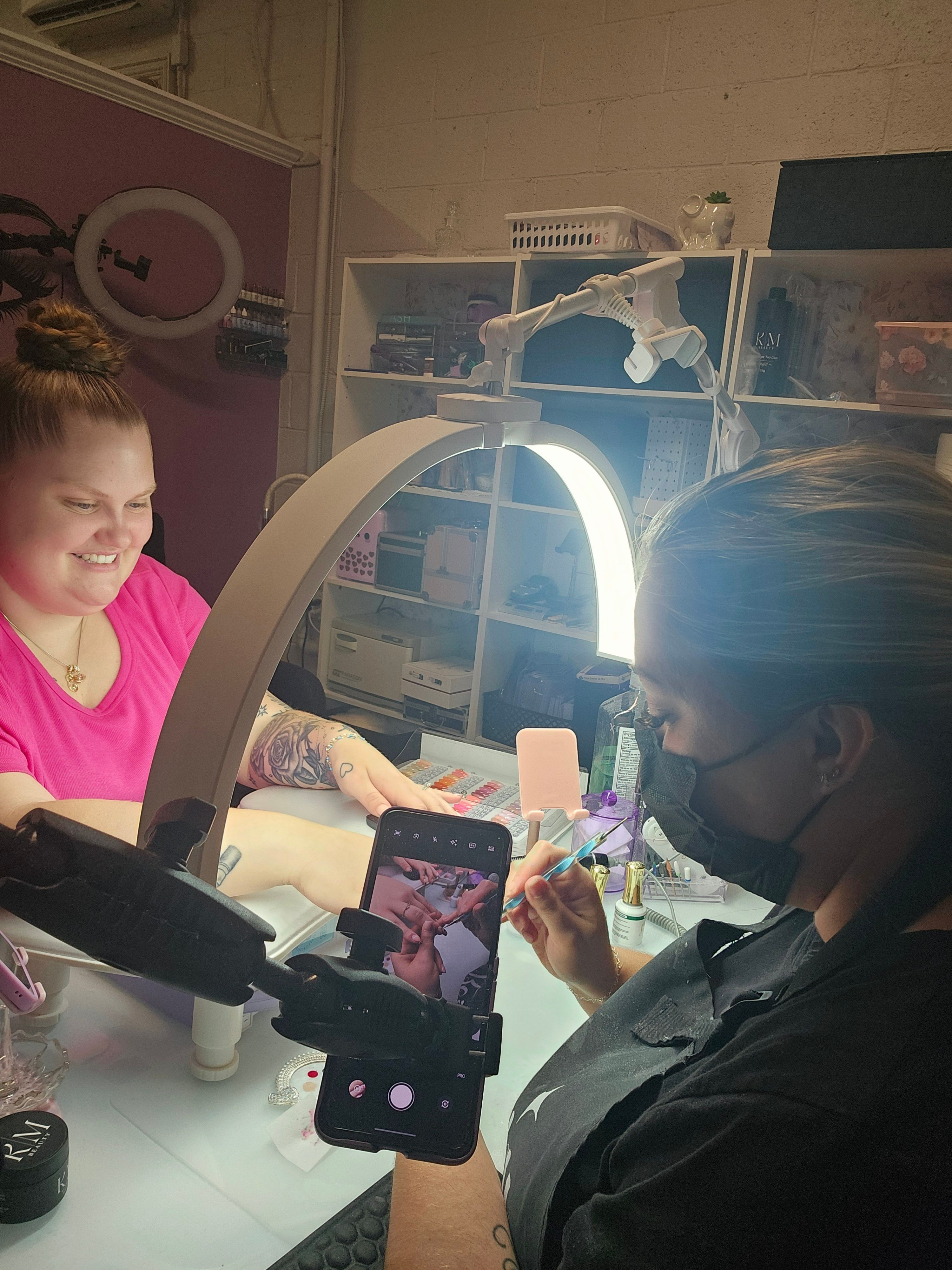 Person taking a mirror selfie with a phone, woman with a pink top, room with shelves and a mirror, bright light.
