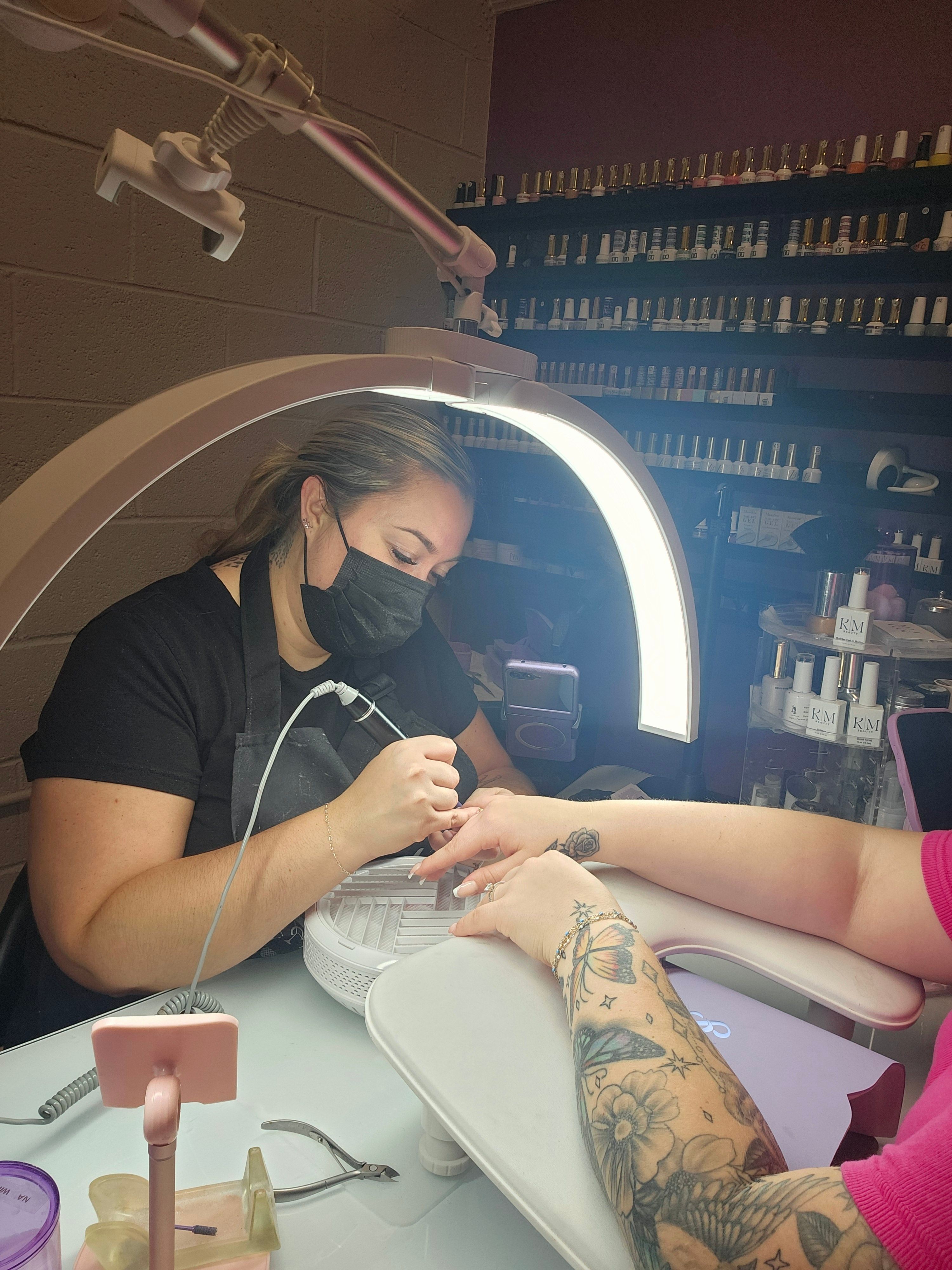 A woman receiving a manicure at a salon, with a technician applying polish, reflected in a mirror, in a well-lit room.