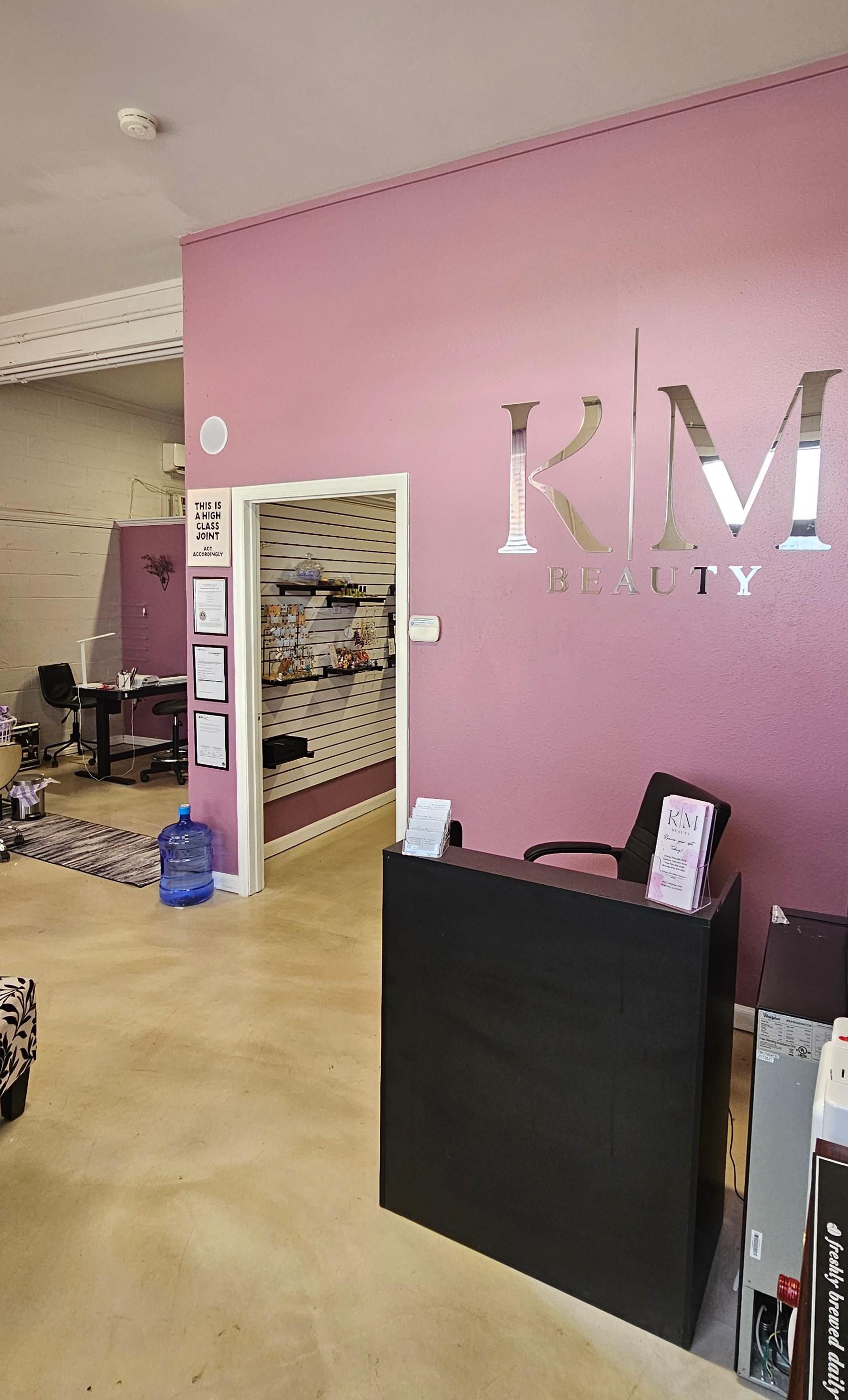 Reception area with pink wall, black desk, and a door leading to a storage room, with office supplies nearby.