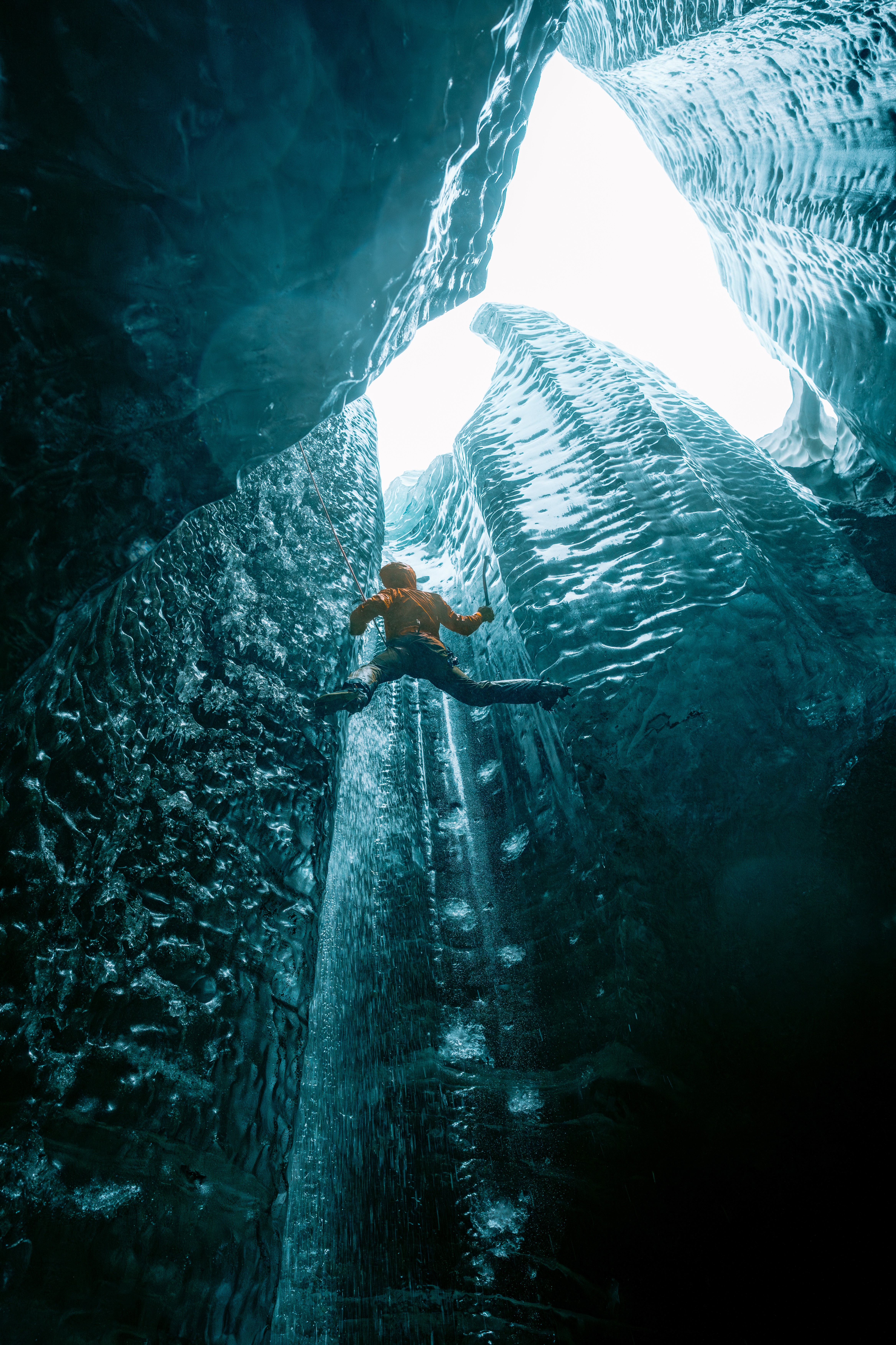Person swimming in a narrow, dark canyon with waterfalls and bright light at the top.