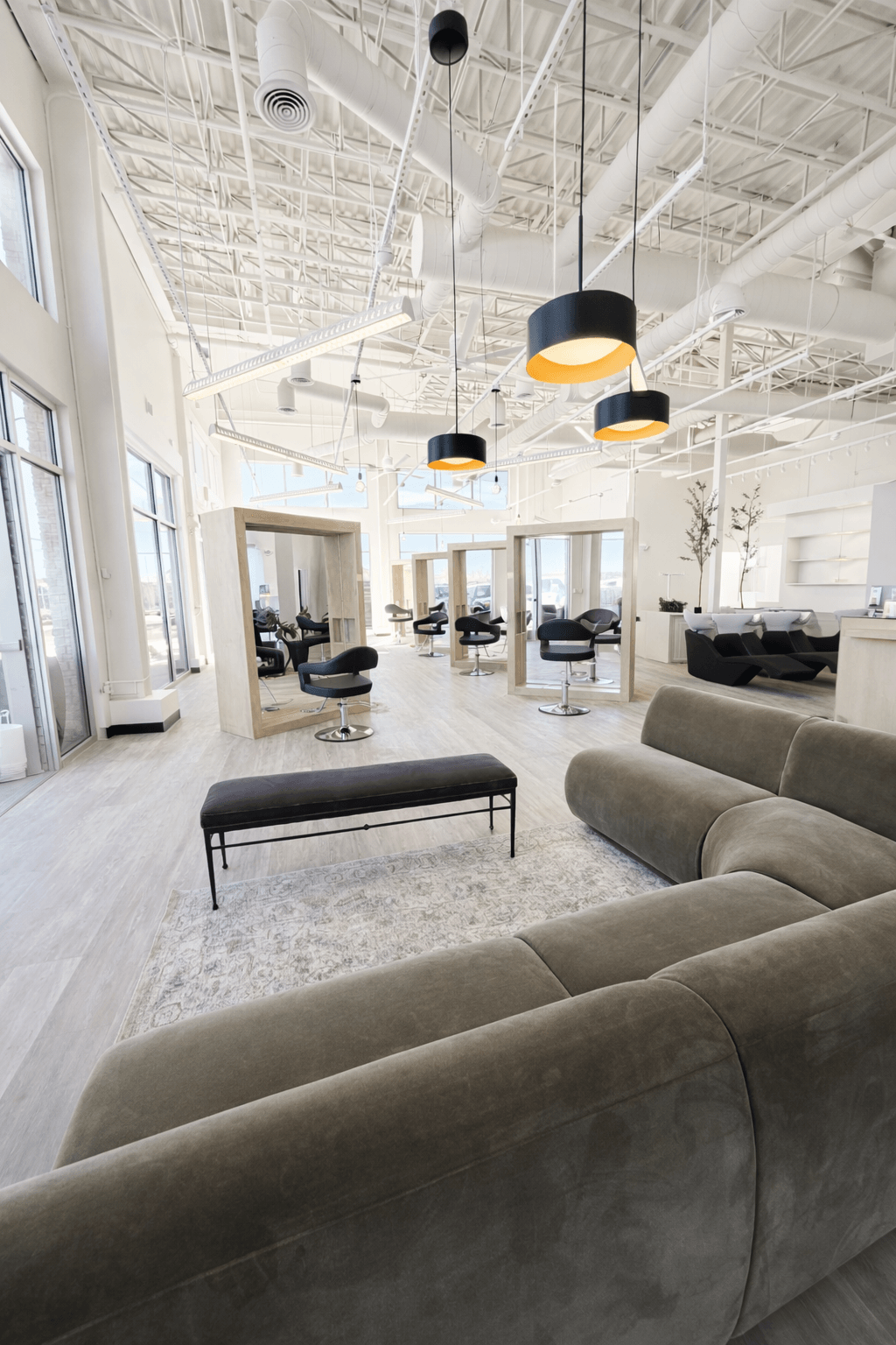 Modern, bright interior with large windows, seating area, and hanging pendant lights, featuring a high ceiling and open space.