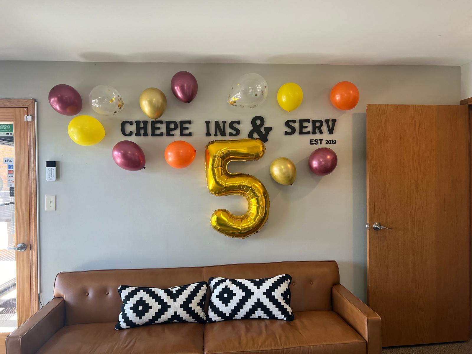 Celebration decorations with balloons and a large gold number five on a wall, with a brown sofa and pillows below.