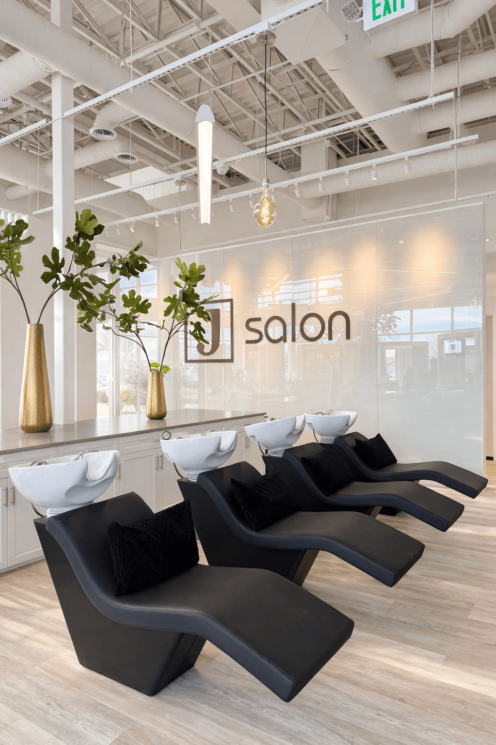 Three black lounge chairs with pillows face a glass wall with salon signage, in a modern salon interior.