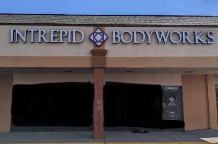 Storefront with sign reading 'INTREPID BODYWORKS' and a logo between the words, beige and brick exterior.