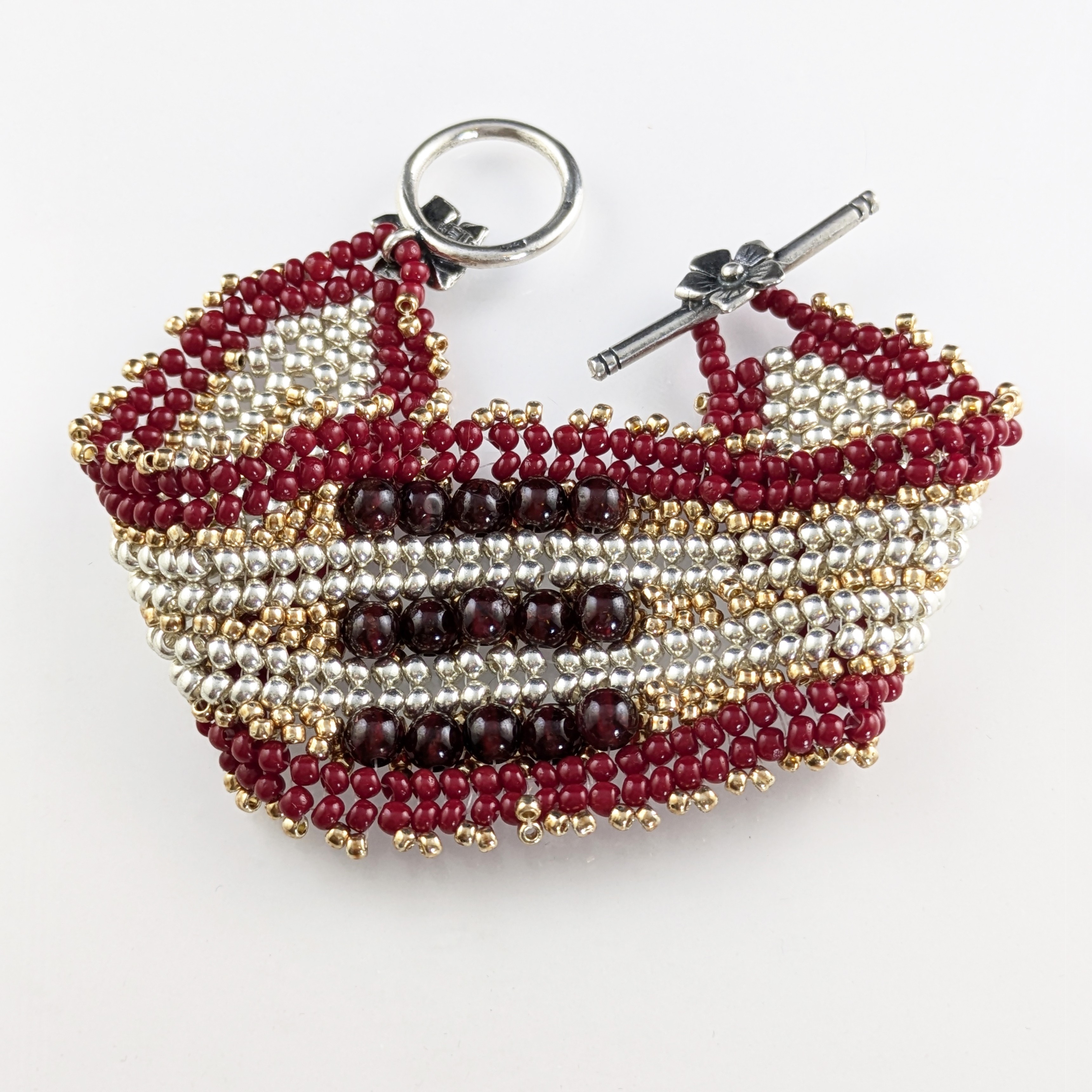 Beaded bracelet with red, white, and black beads, featuring a keyring and a pin, on a white background.