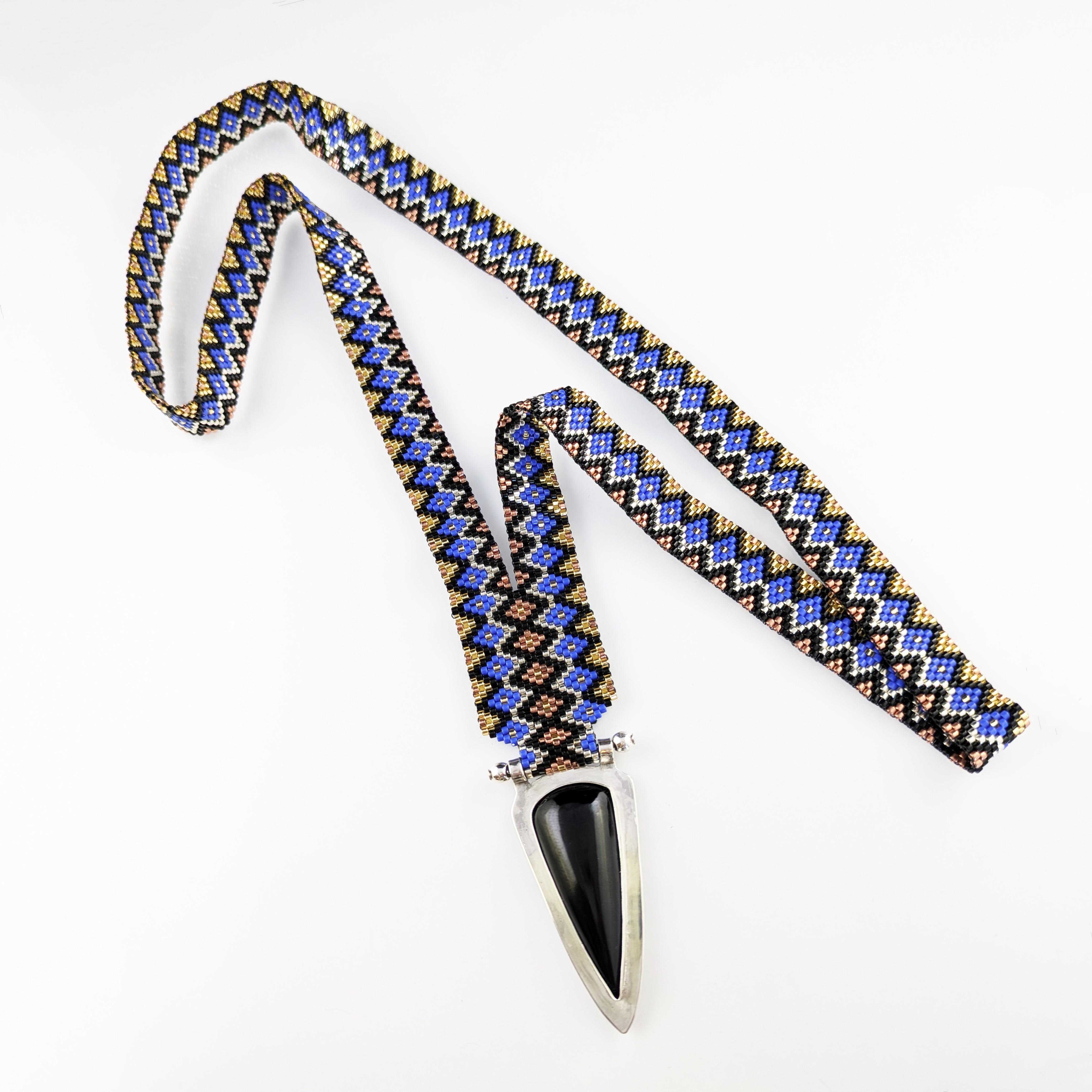 Necklace with a black and silver pendant on a zigzag patterned fabric cord, laid flat on a white background.