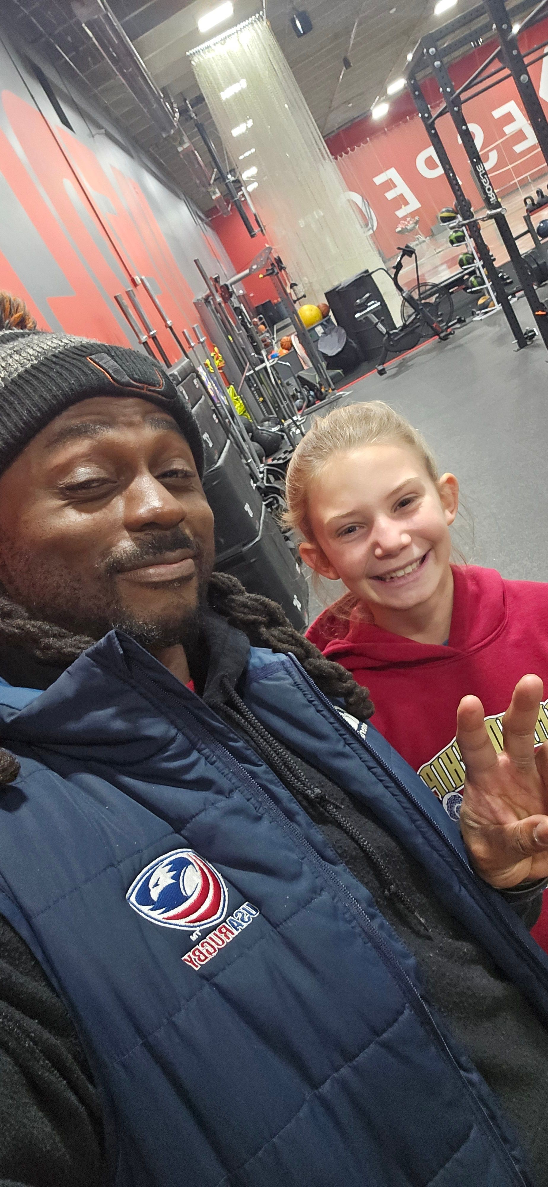 Two people taking a selfie inside a building, one wearing a red top and the other in a dark jacket, smiling.