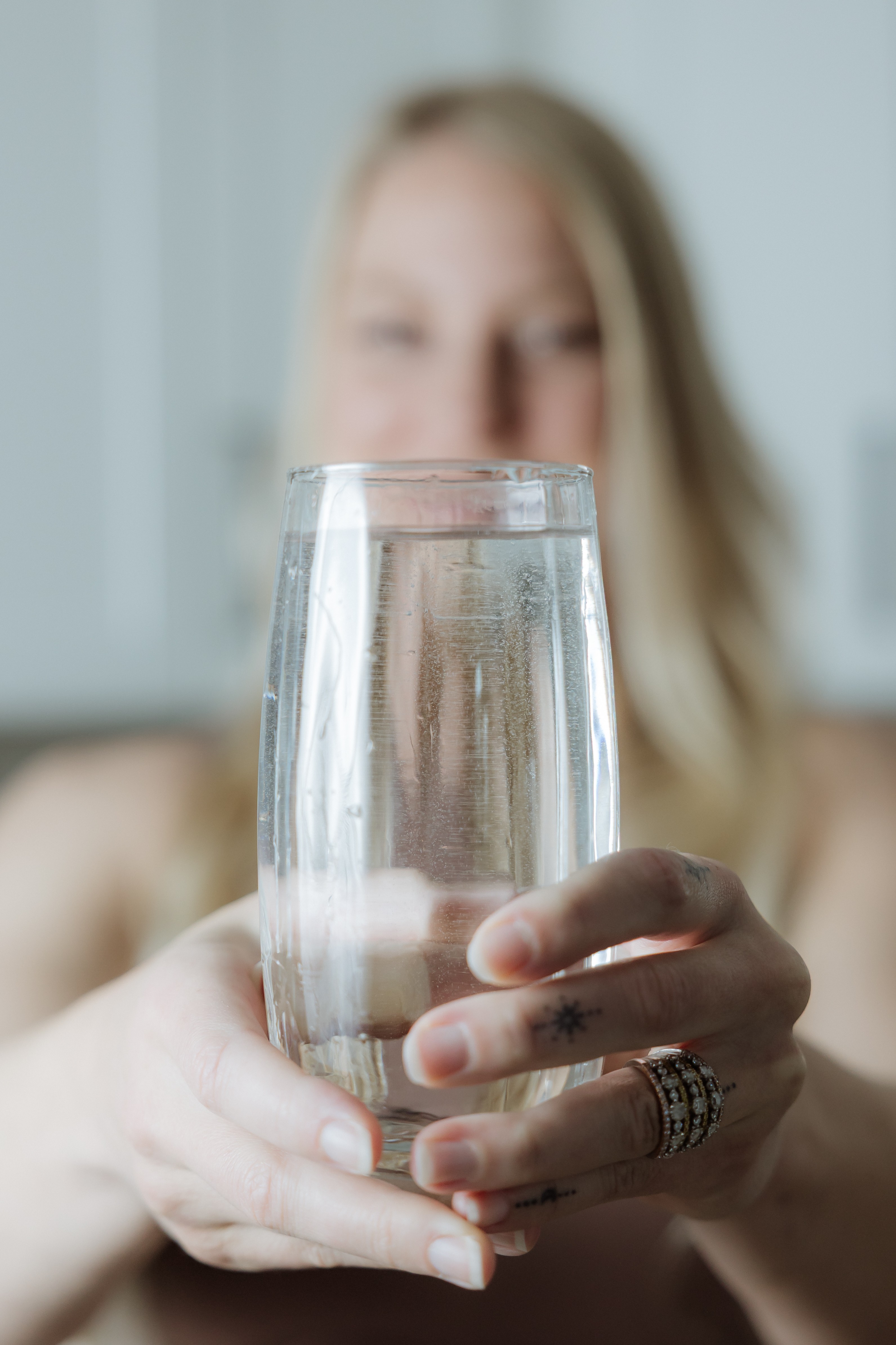 Person holding a glass of water, with blurred face and background, focus on the glass.
