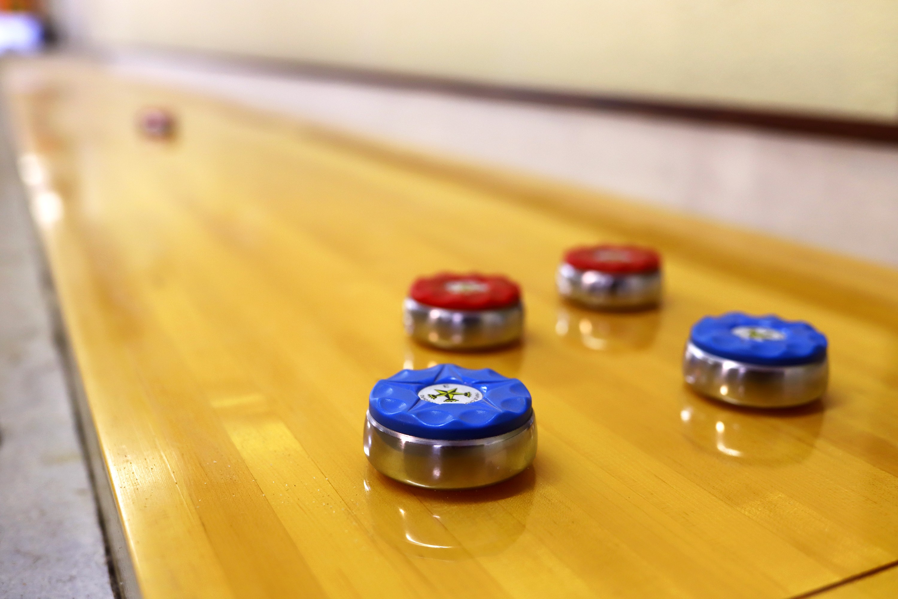 Four curling stones on a wooden curling rink, two with red handles and two with blue handles.