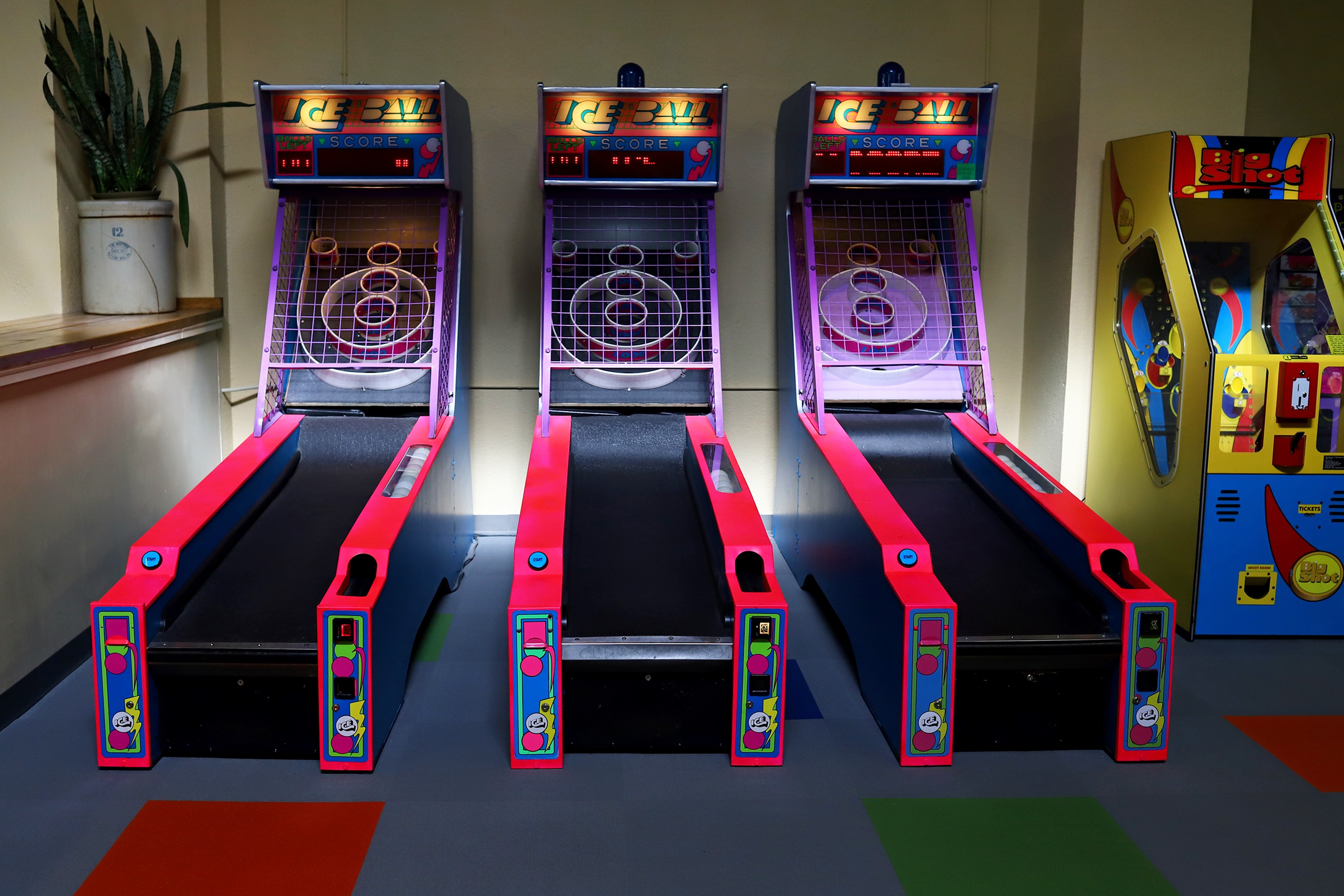 Three arcade skee-ball machines with purple targets and red lanes, and a yellow and blue coin pusher game on the right.