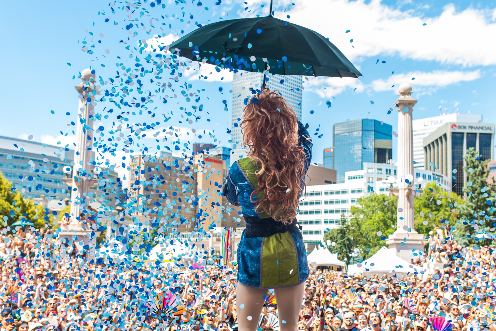 Person with long hair holding an umbrella, surrounded by colorful confetti in an urban park setting.