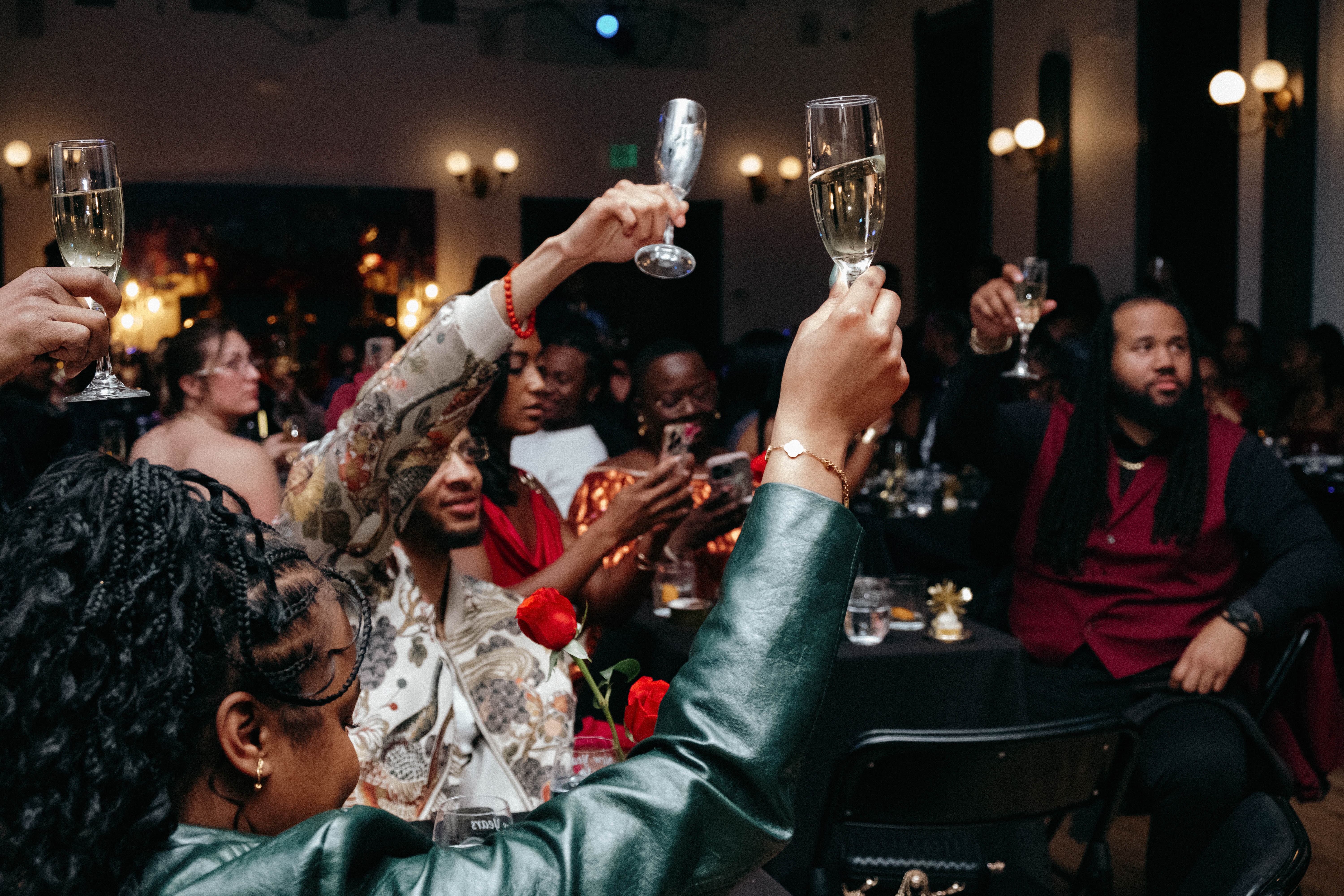 People celebrating with champagne glasses raised in a dimly lit party setting, smiling and enjoying the event.