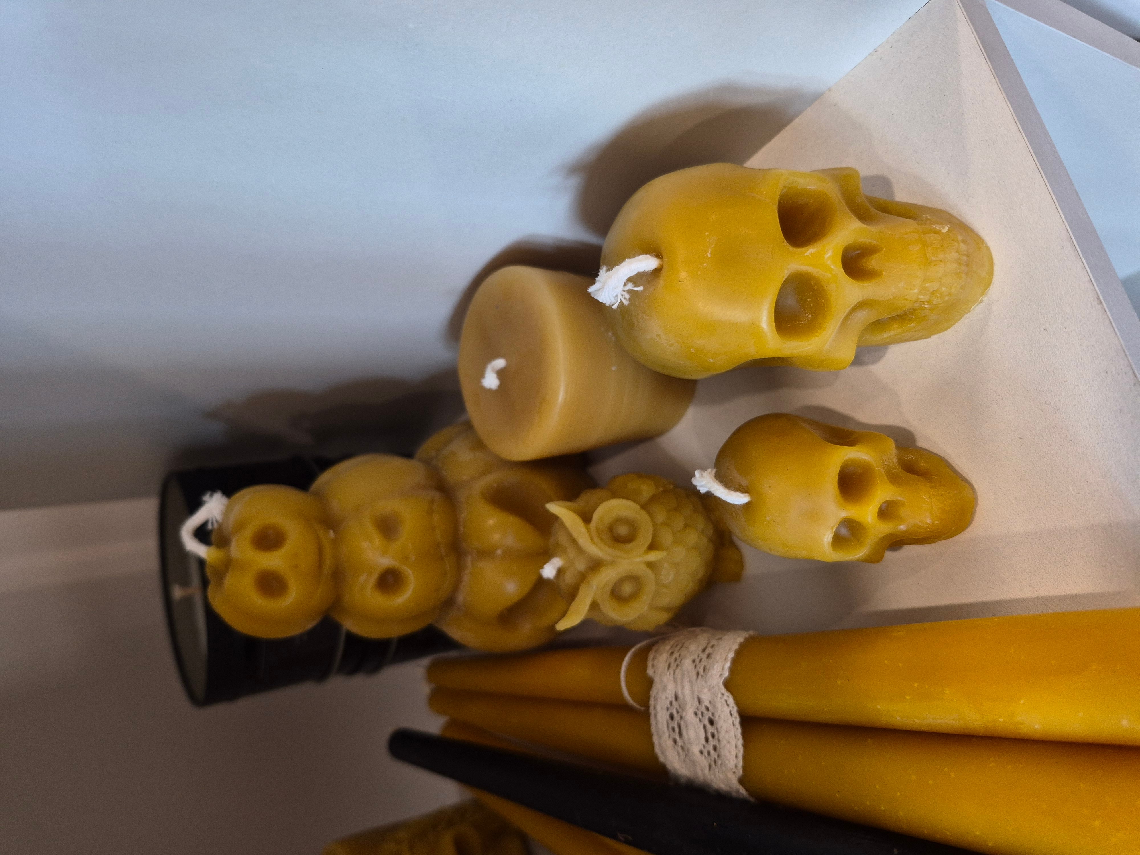 Collection of candles shaped like skulls and other objects, with a bundle of yellow candles tied with lace, on a surface.