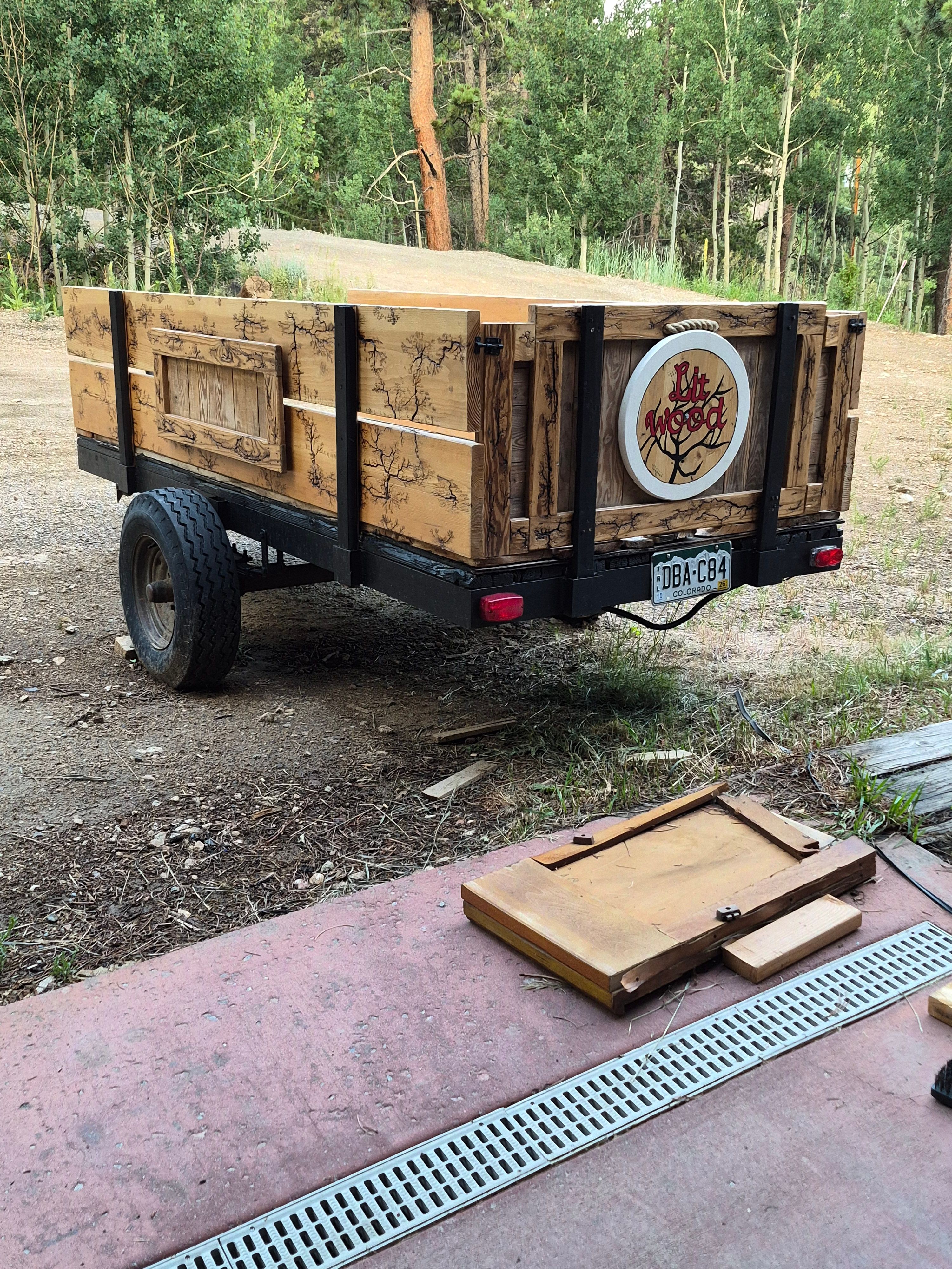 Wooden food cart with a logo of a tree, set outdoors with trees in the background, on a dirt ground.