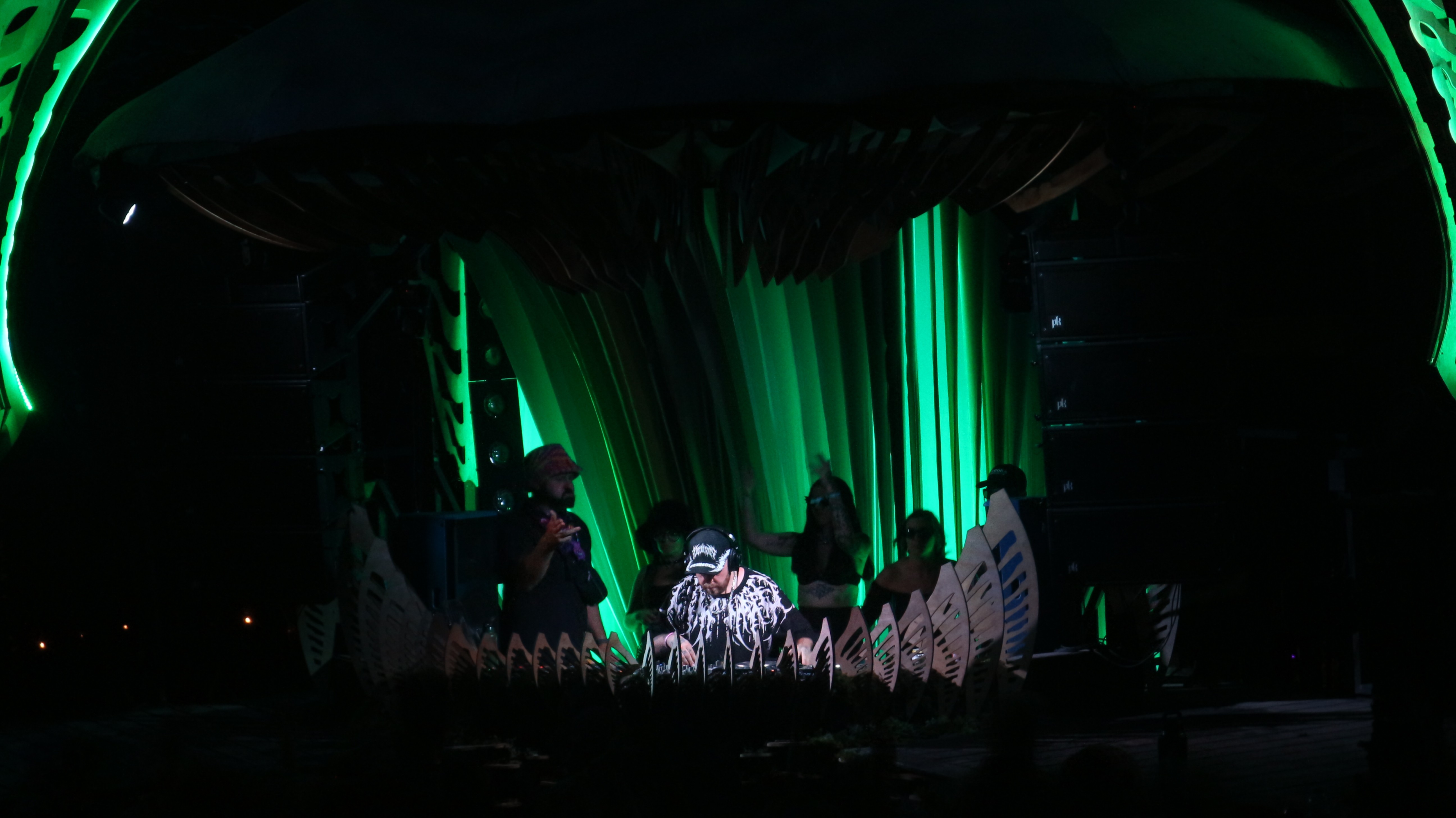 Stage with green lighting, performers, and a backdrop of vertical green light beams, with a dark surrounding environment.