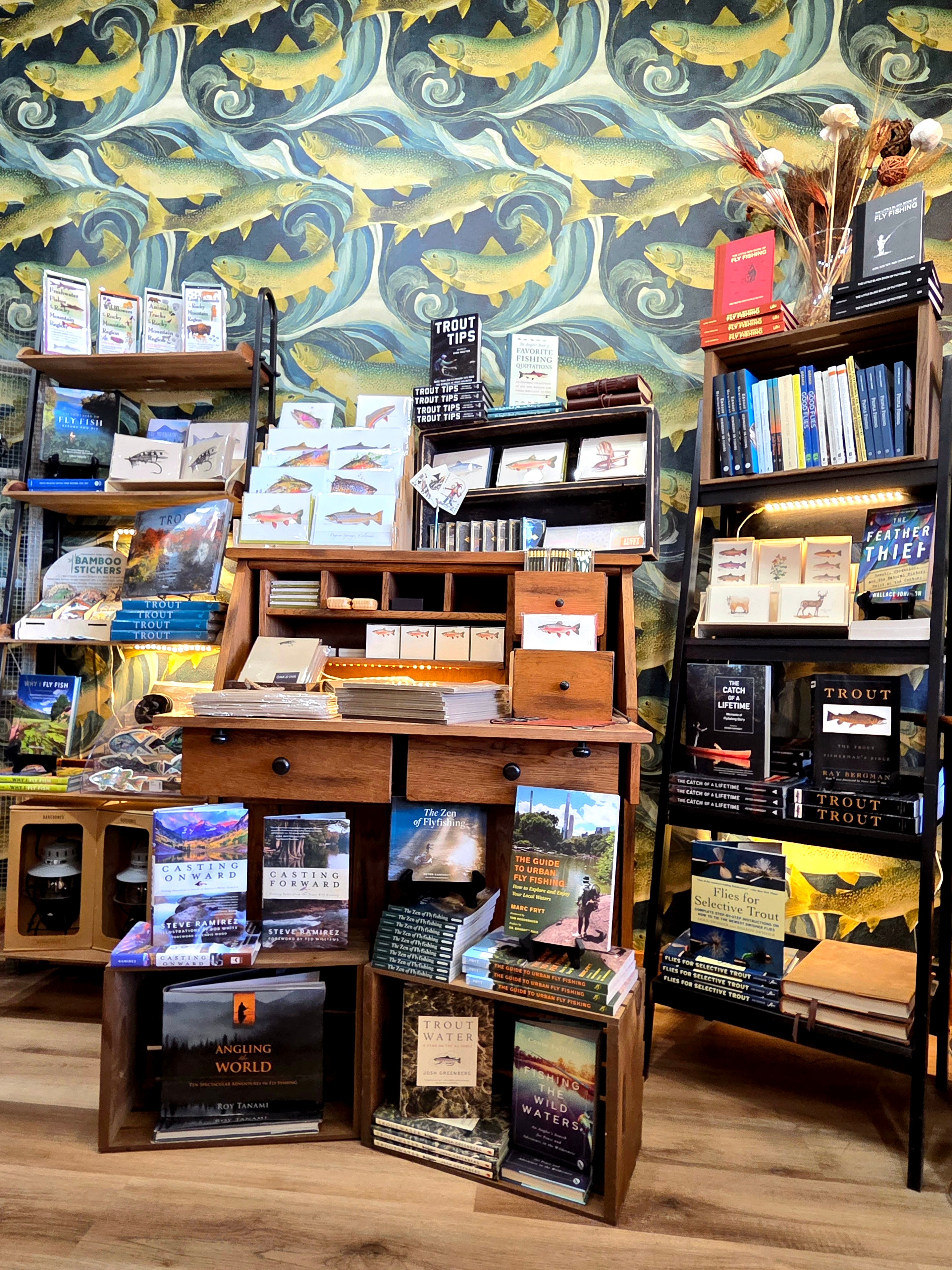 Bookshelves filled with books and magazines in front of a colorful, ocean-themed wallpaper. Wooden floor visible.