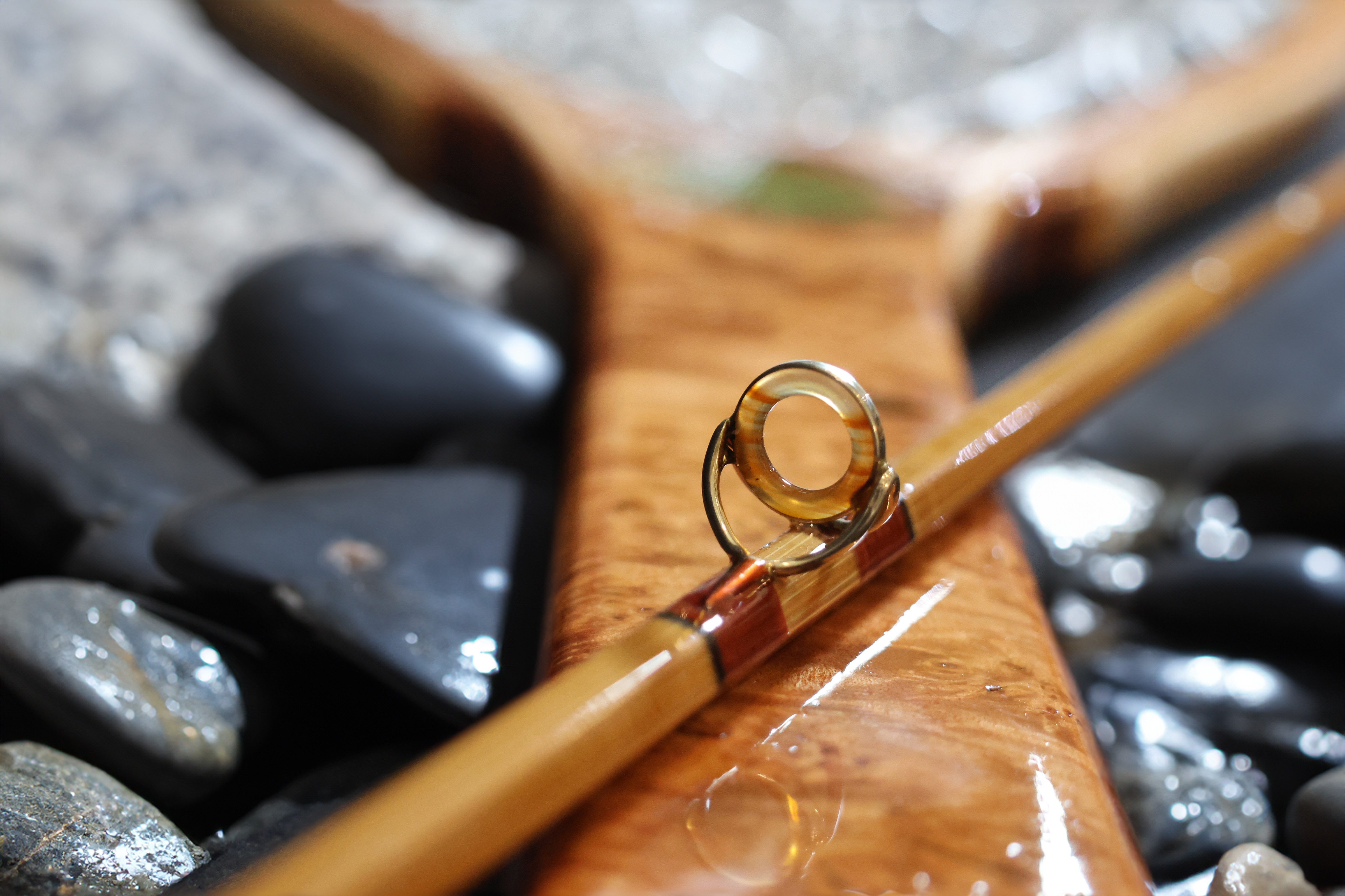 Close-up of a fishing rod with a water droplet on it, surrounded by smooth stones and a wooden Y-shaped stick.