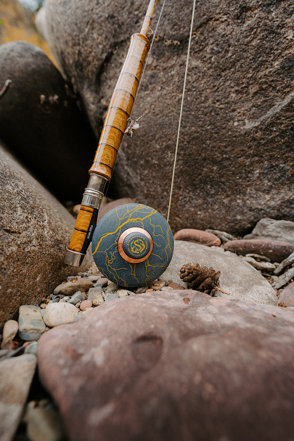 Fishing rod and ball on rocks near water, with rocks and water in background.