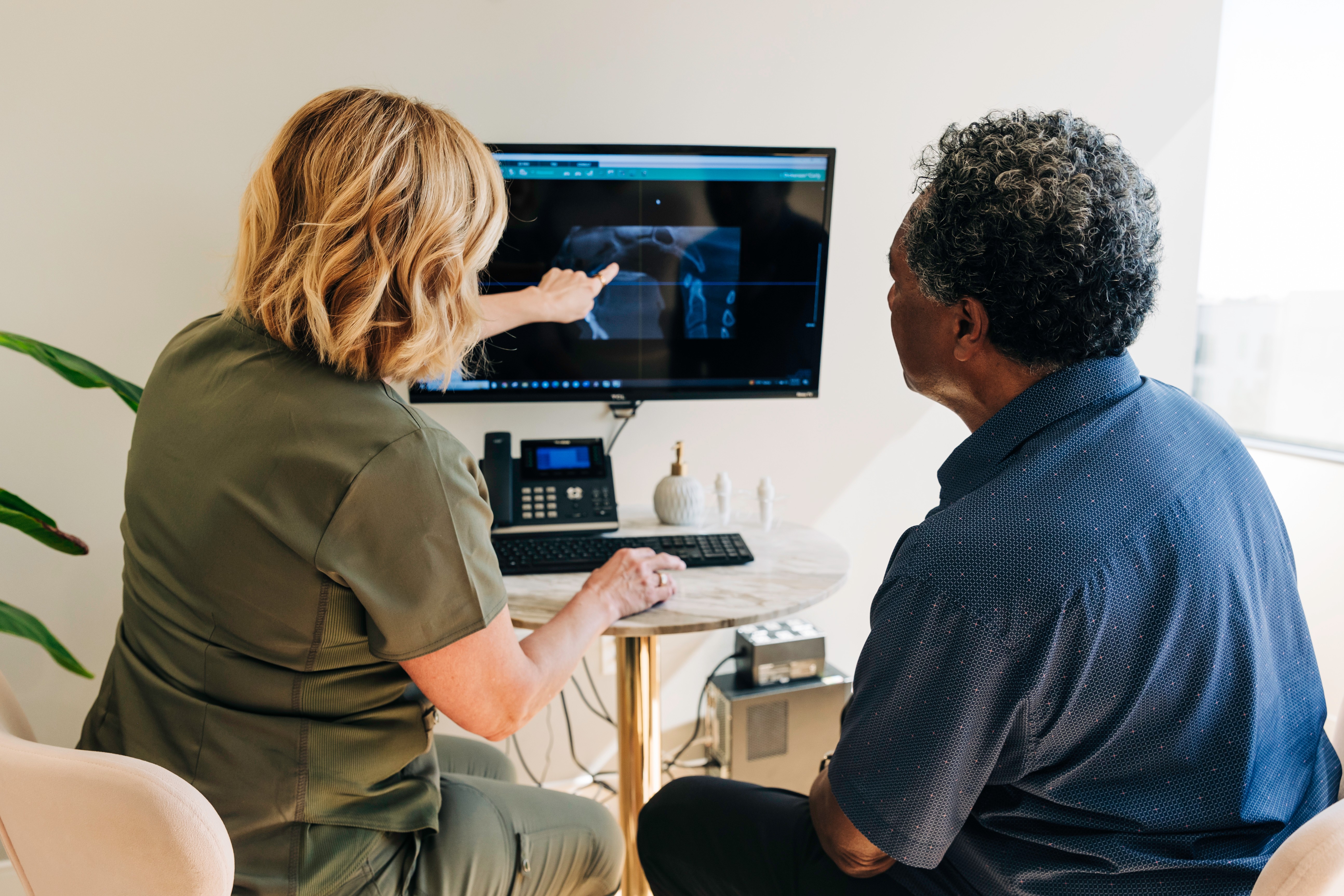 Two people, a woman and a man, sit in front of a computer monitor displaying a medical scan, engaging in discussion.