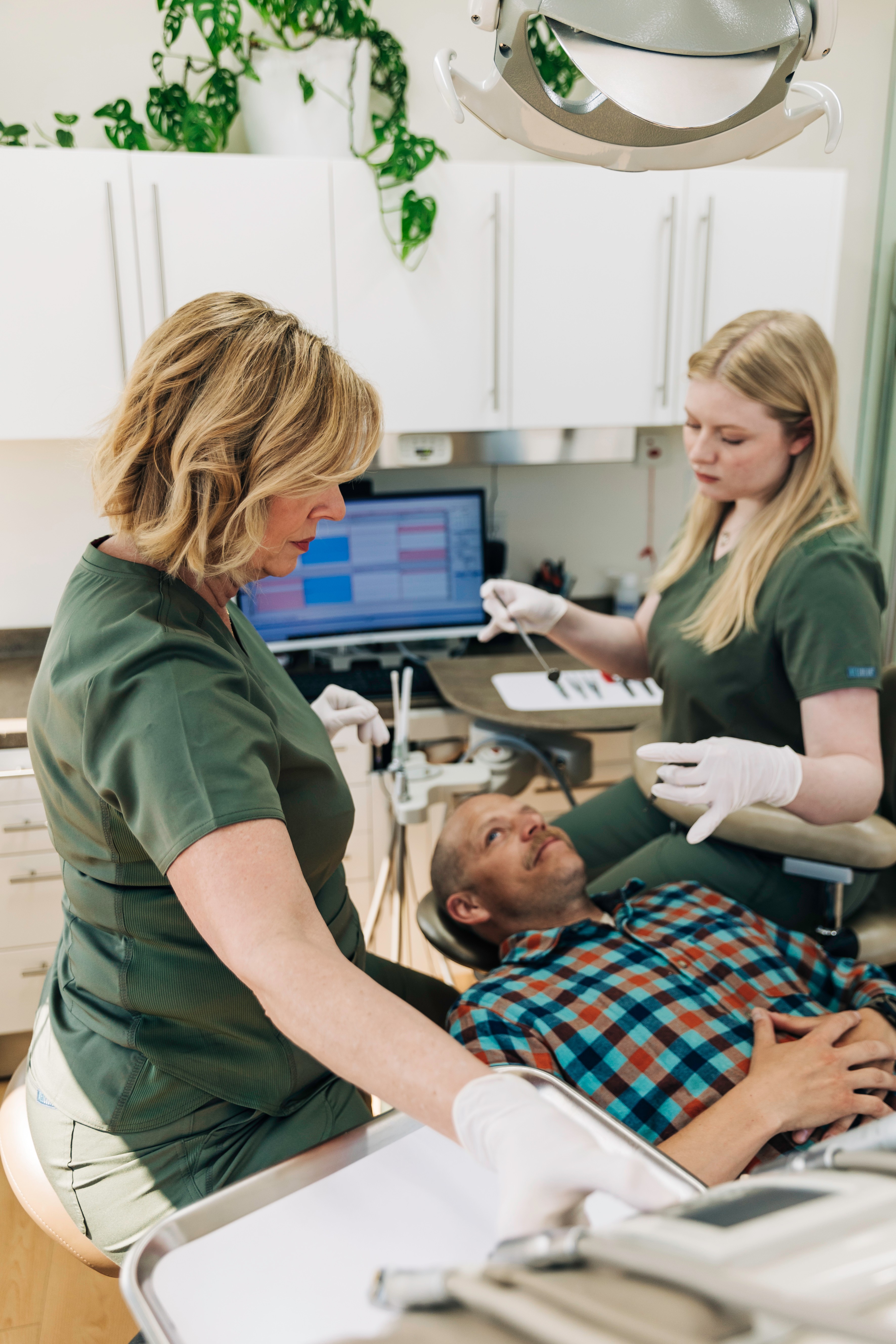 A woman lying on a medical chair with a plaid shirt, two healthcare professionals attending, one with a laptop, in a clinical setting.