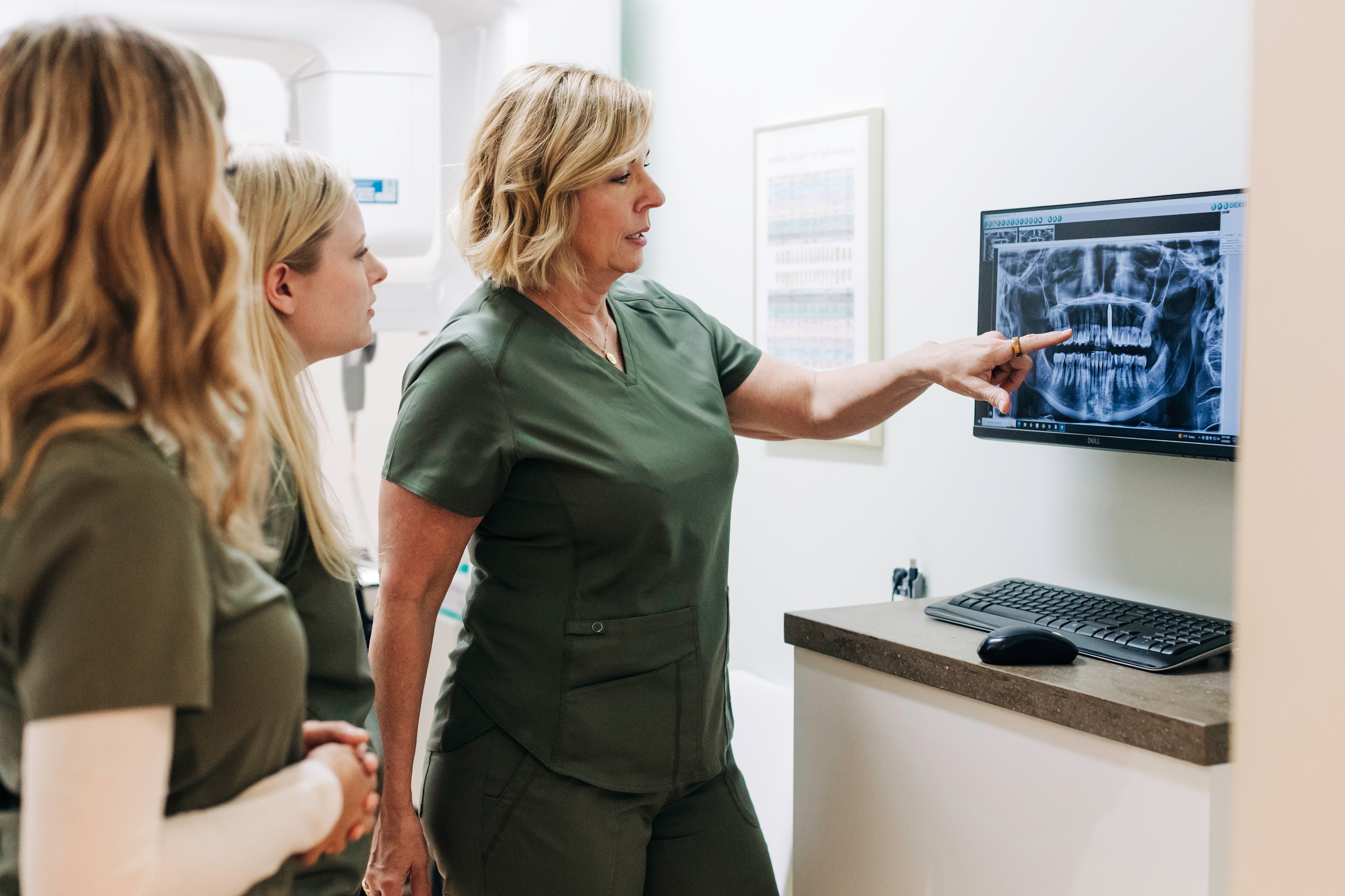 Dental professional showing dental X-ray on screen to three women in a clinic room.
