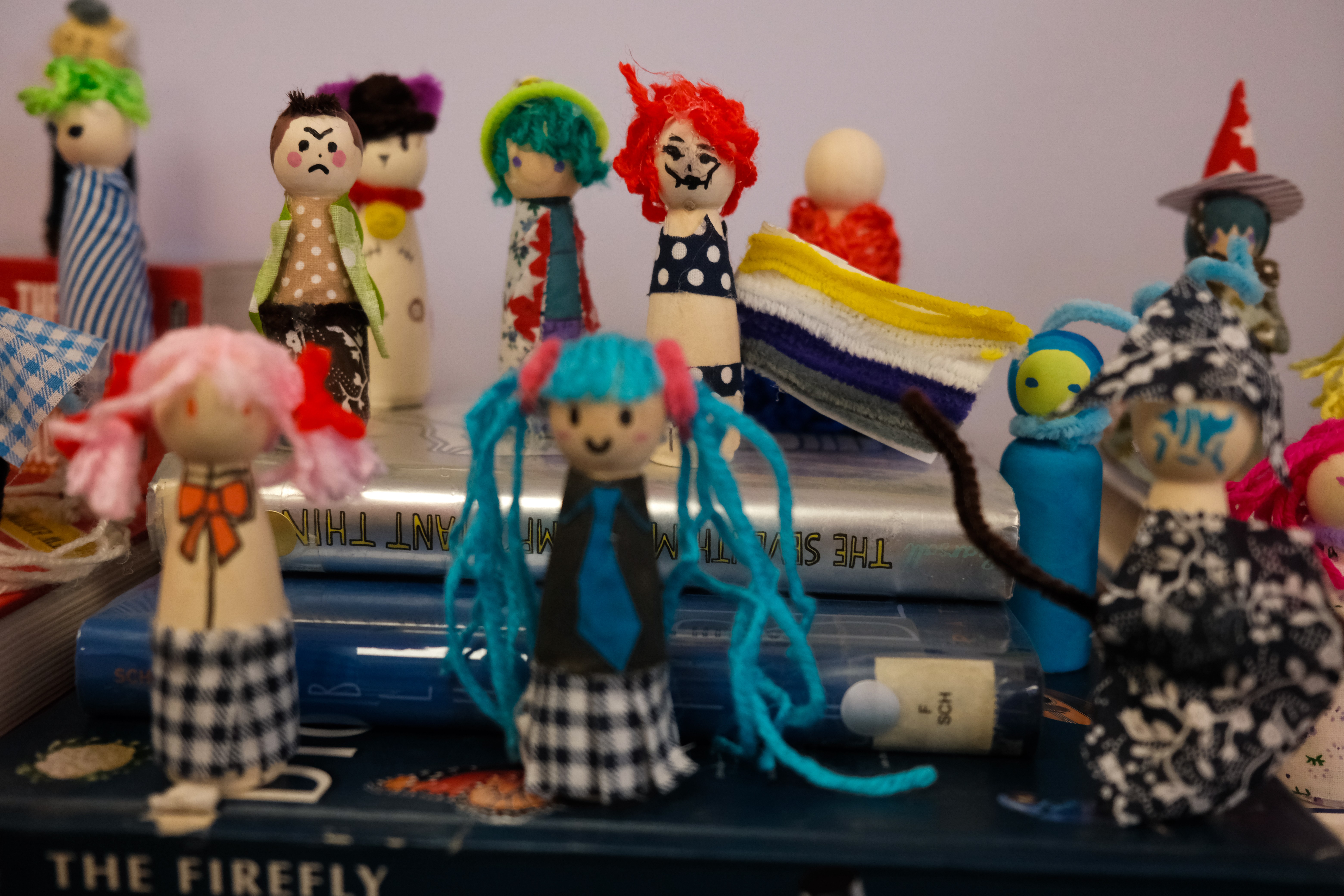 Collection of colorful handmade dolls with various hairstyles and outfits, displayed on a surface with pens and papers nearby.