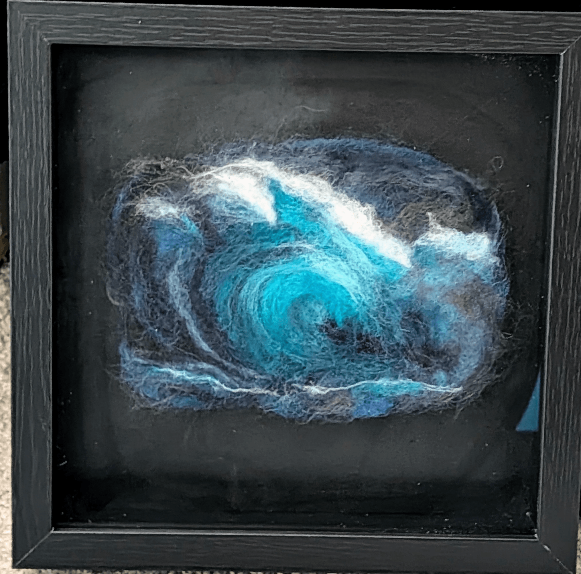 Abstract swirling blue and white pattern resembling a galaxy or vortex, framed in black. Word count: 20.