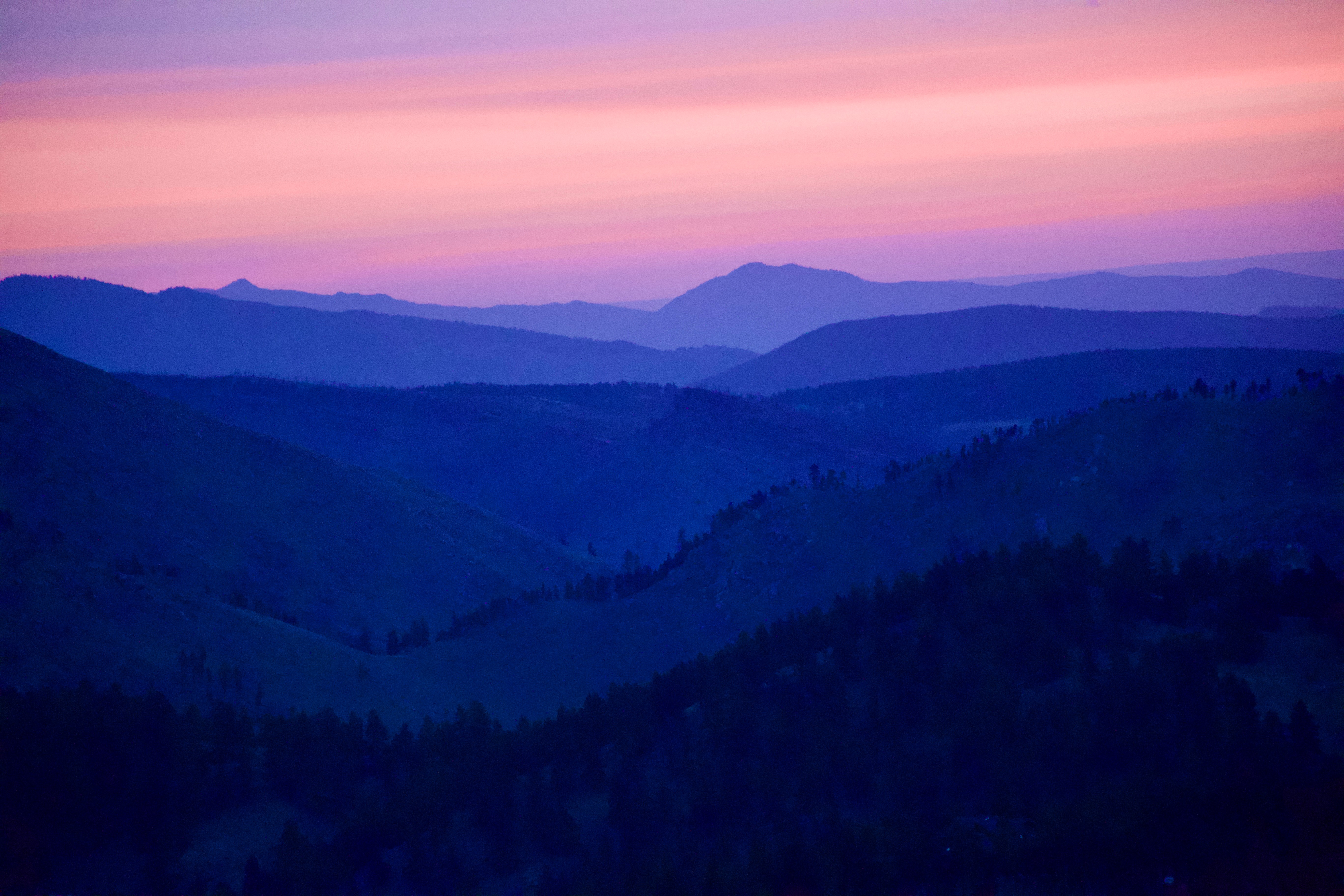 Layered mountain ranges under a pink and purple sky at sunset or sunrise.