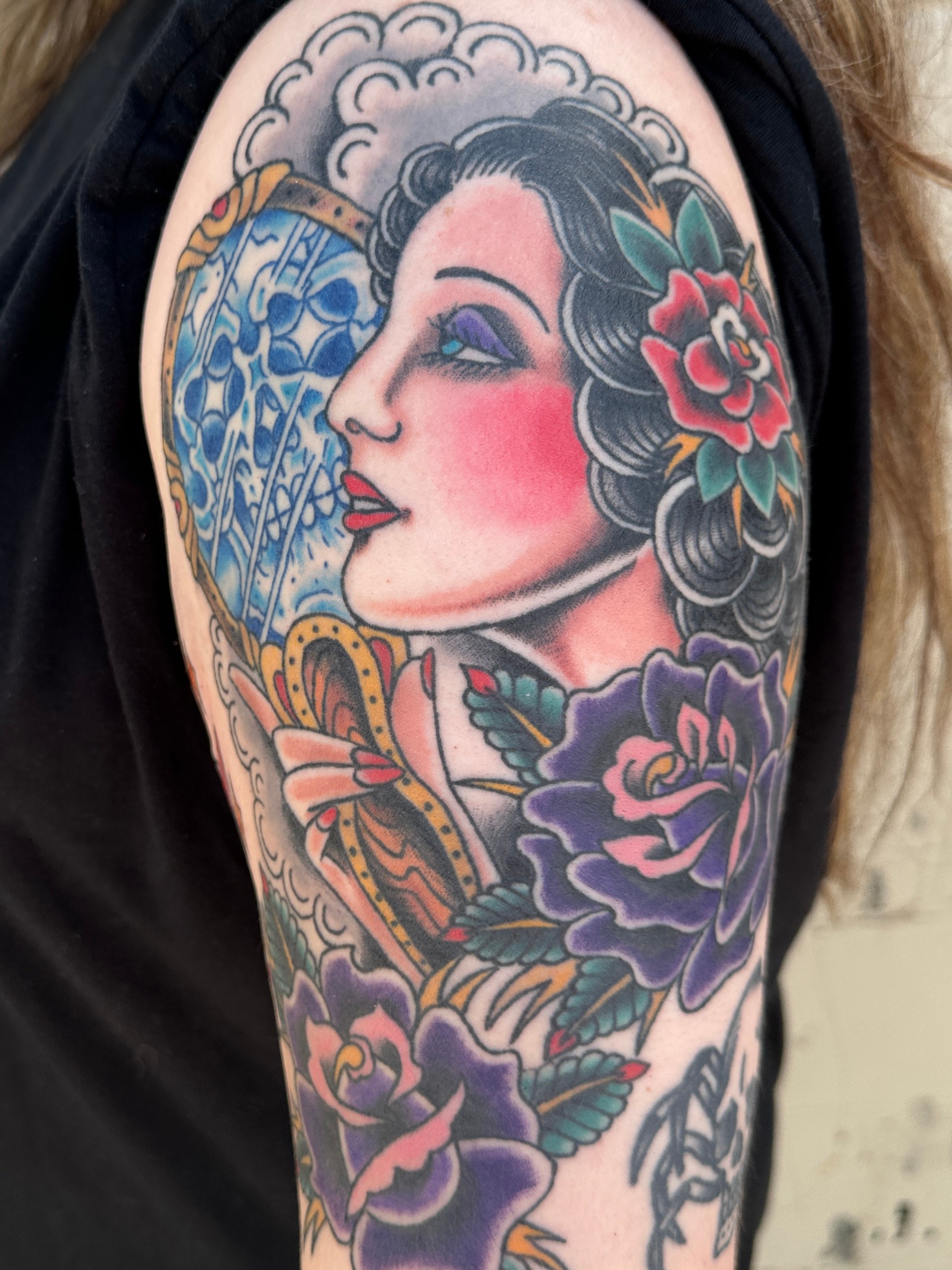 Tattoo of a woman's face with colorful flowers and clouds on her shoulder, detailed and vibrant.