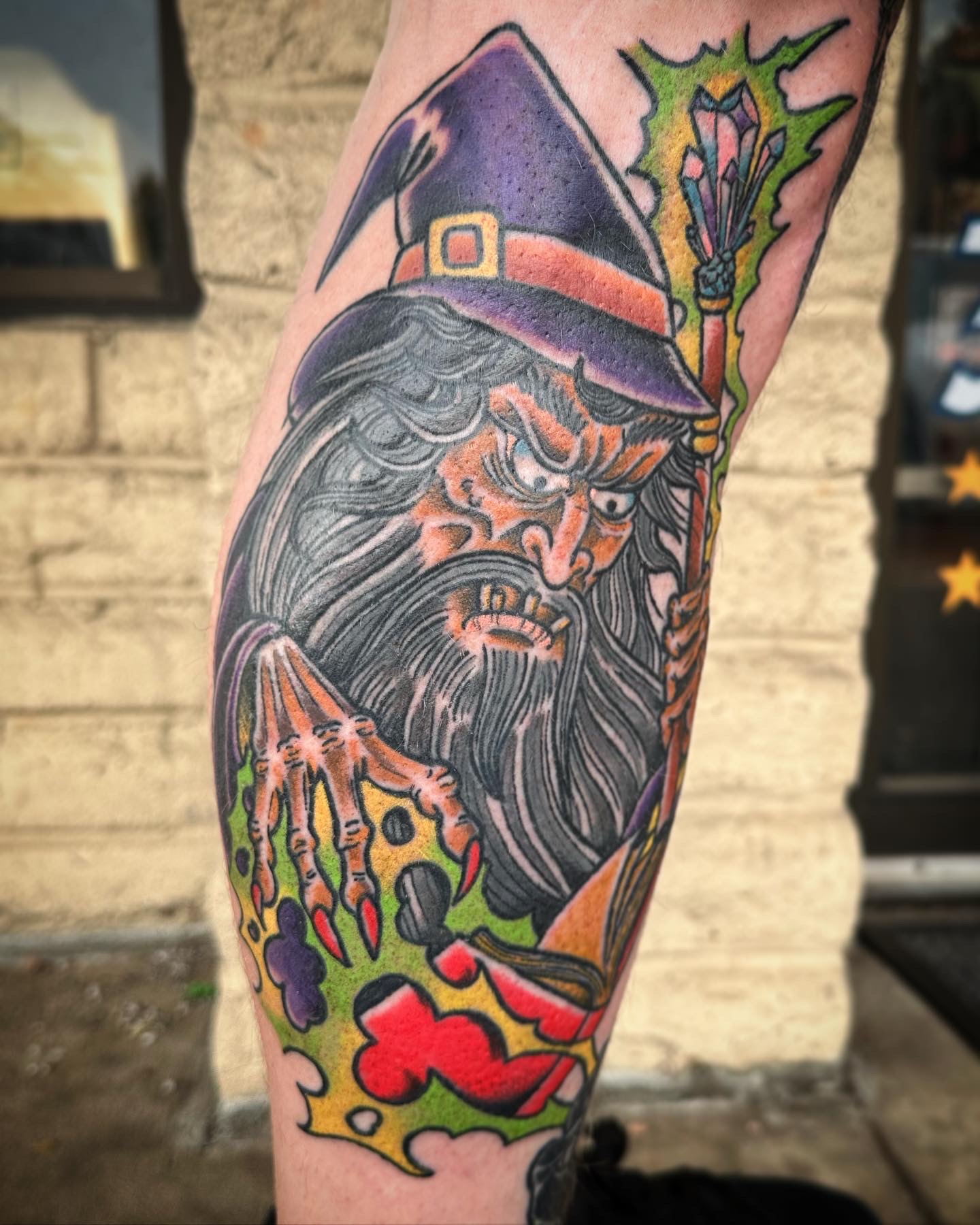 Tattoo of a wizard with a long beard and hat, holding a staff, surrounded by colorful abstract elements.