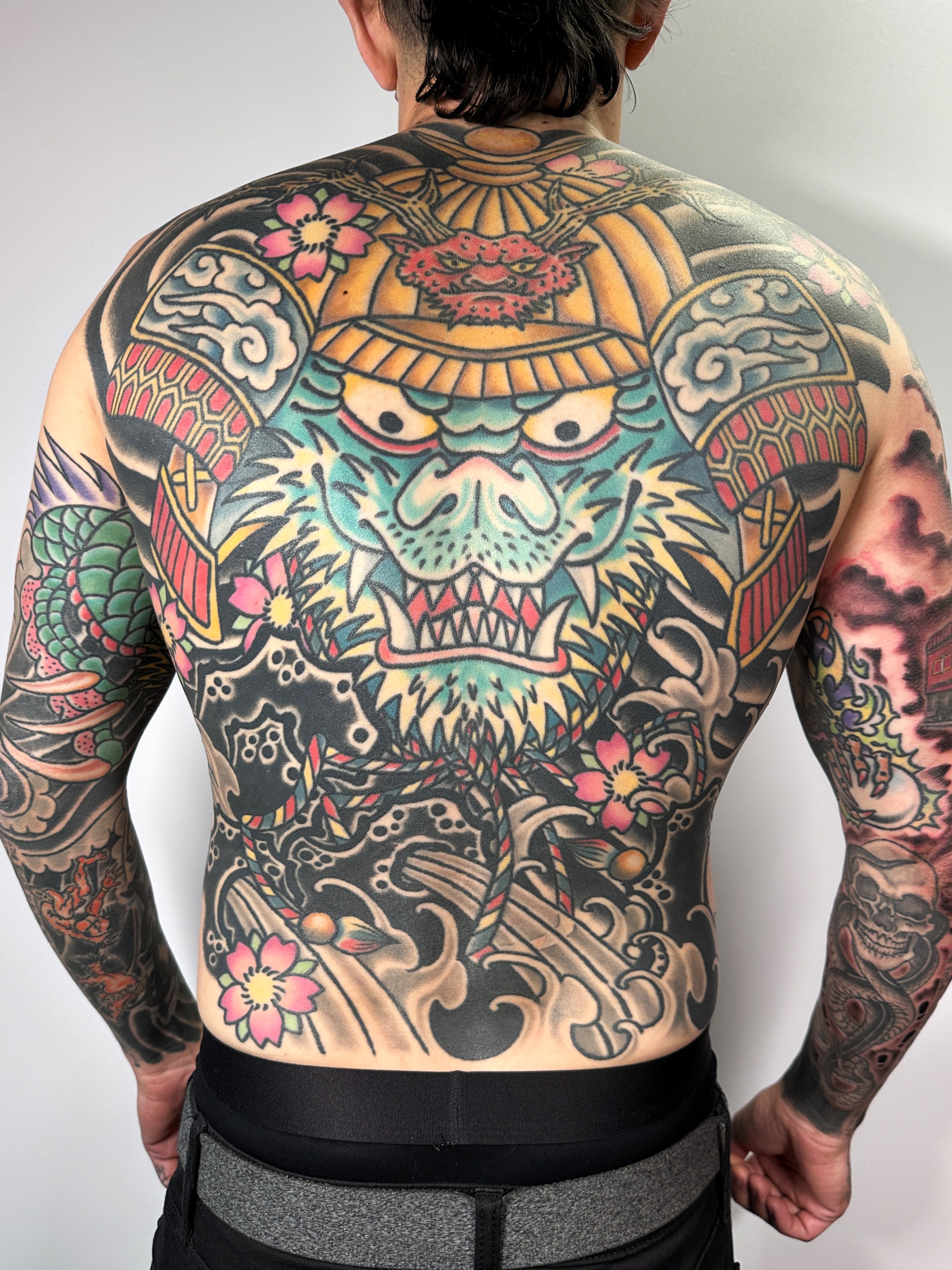 Back tattoo featuring a large, colorful creature with a fierce expression, surrounded by floral and wave patterns.