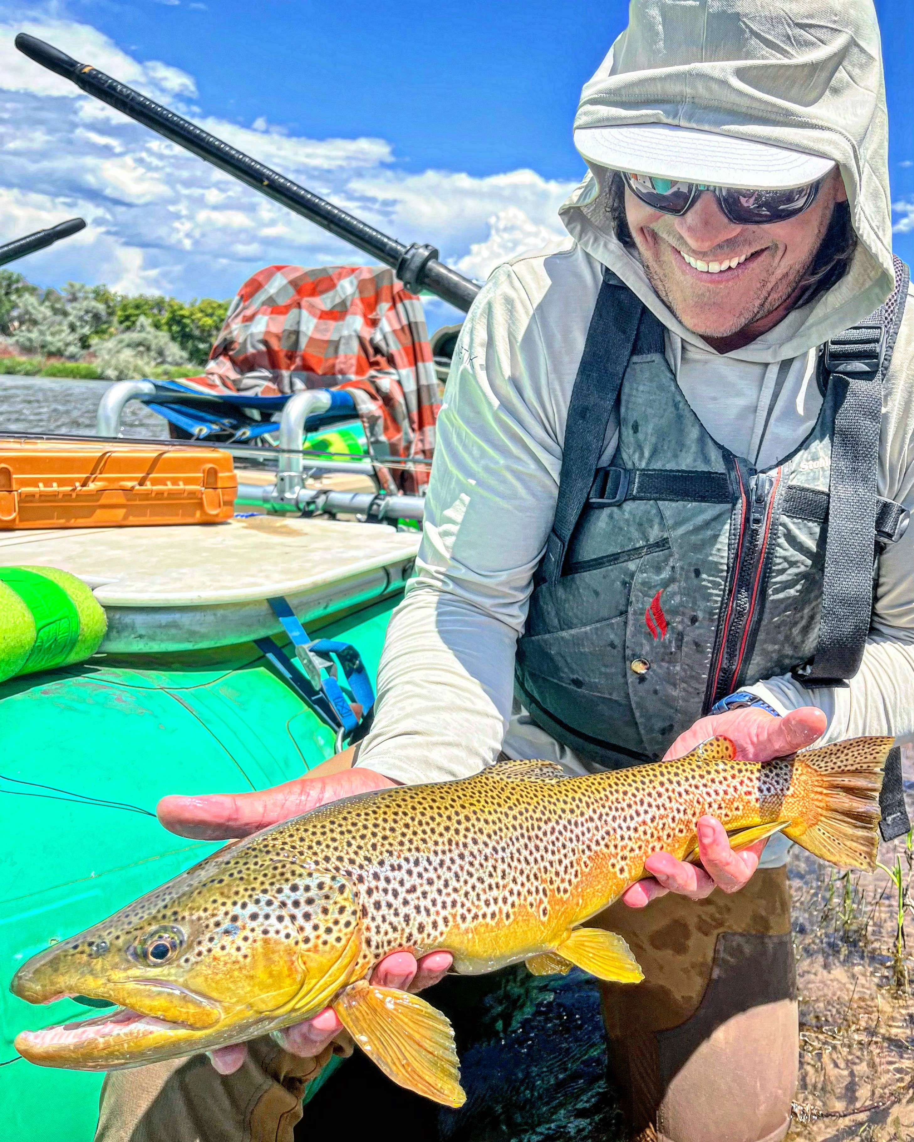 Person holding a large fish outdoors with fishing gear and a blue sky in background.